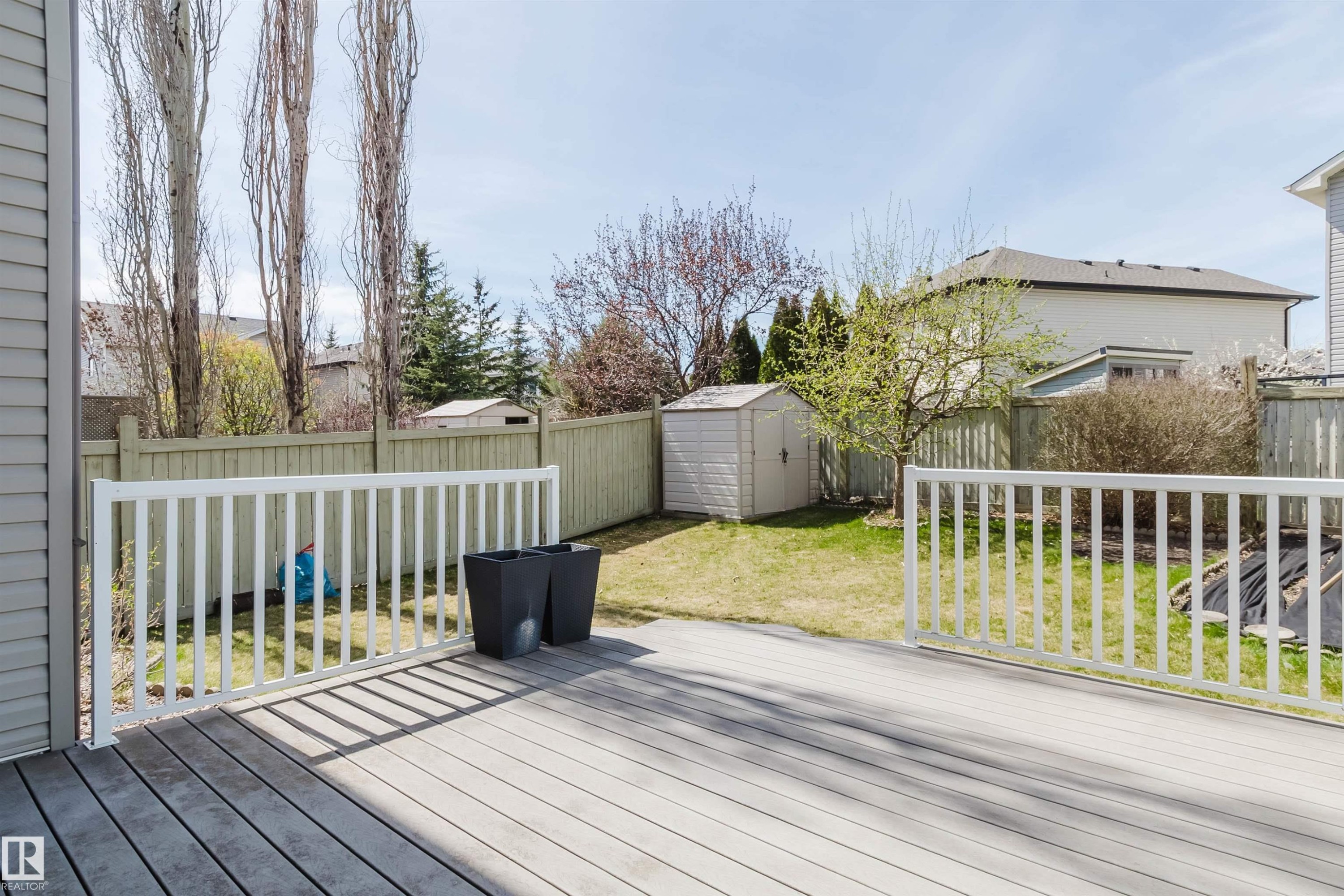 Spacious outdoor deck featuring light-toned composite decking and white railing, overlooking a fenced backyard with a lawn and storage shed - 1140 115 Street, Edmonton, AB - Outdoor With Deck Patio Veranda With Exterior