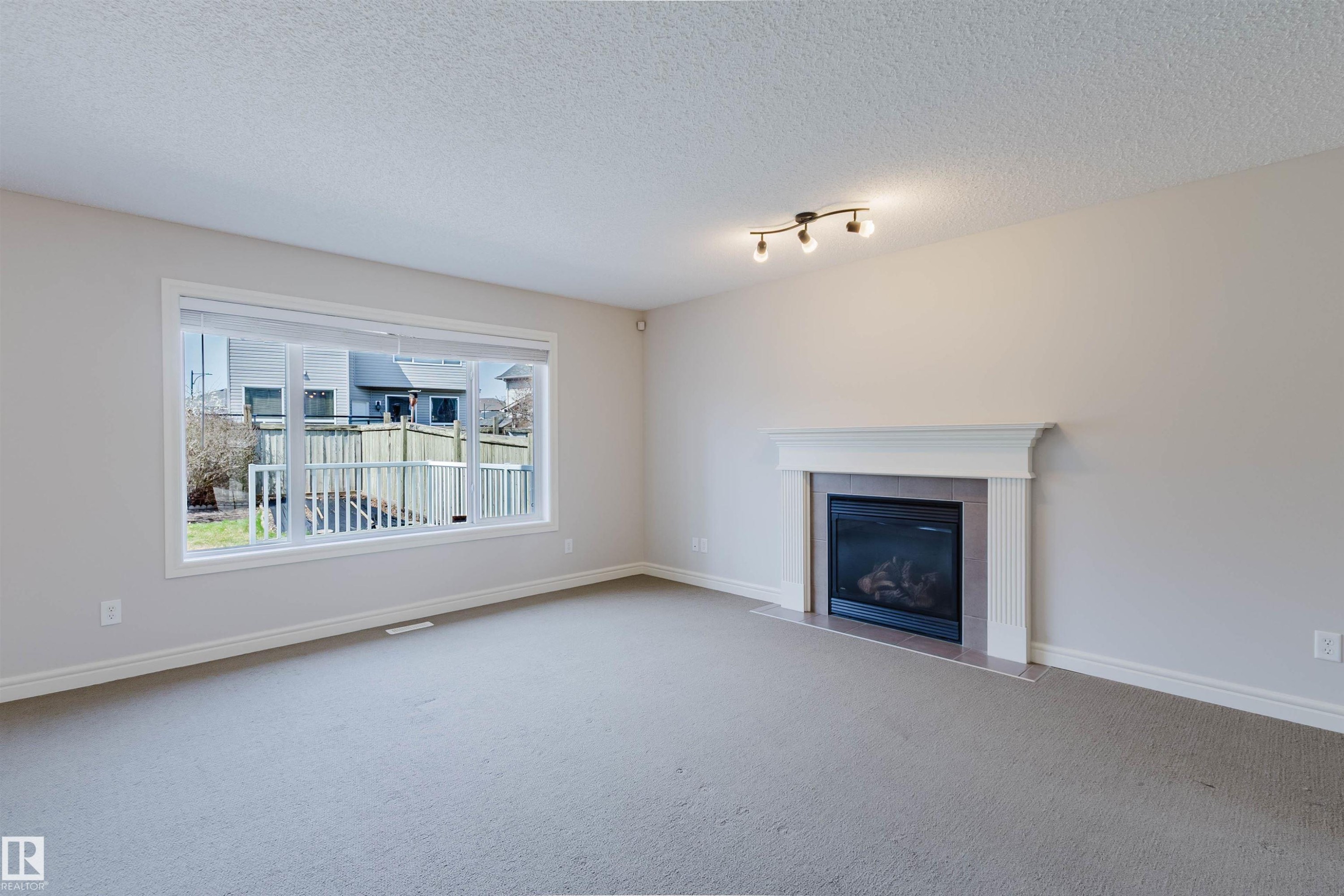Living area featuring a fireplace with a white mantel, an expansive window, light-colored walls, and track lighting - 1140 115 Street, Edmonton, AB - Indoor Photo Showing Living Room With Fireplace