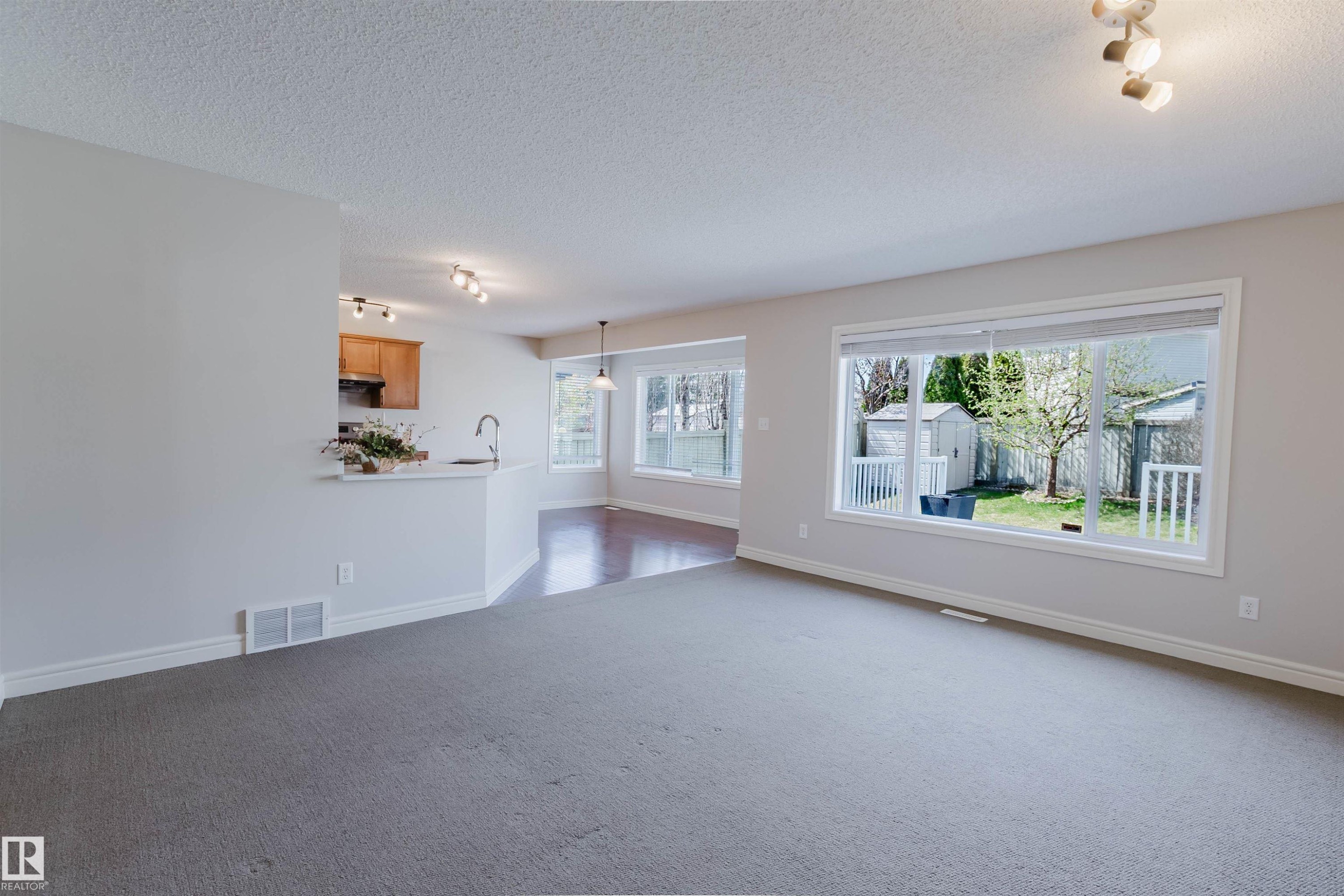 Spacious living area featuring neutral carpeting, a large picture window, and a built-in breakfast bar - 1140 115 Street, Edmonton, AB - Indoor