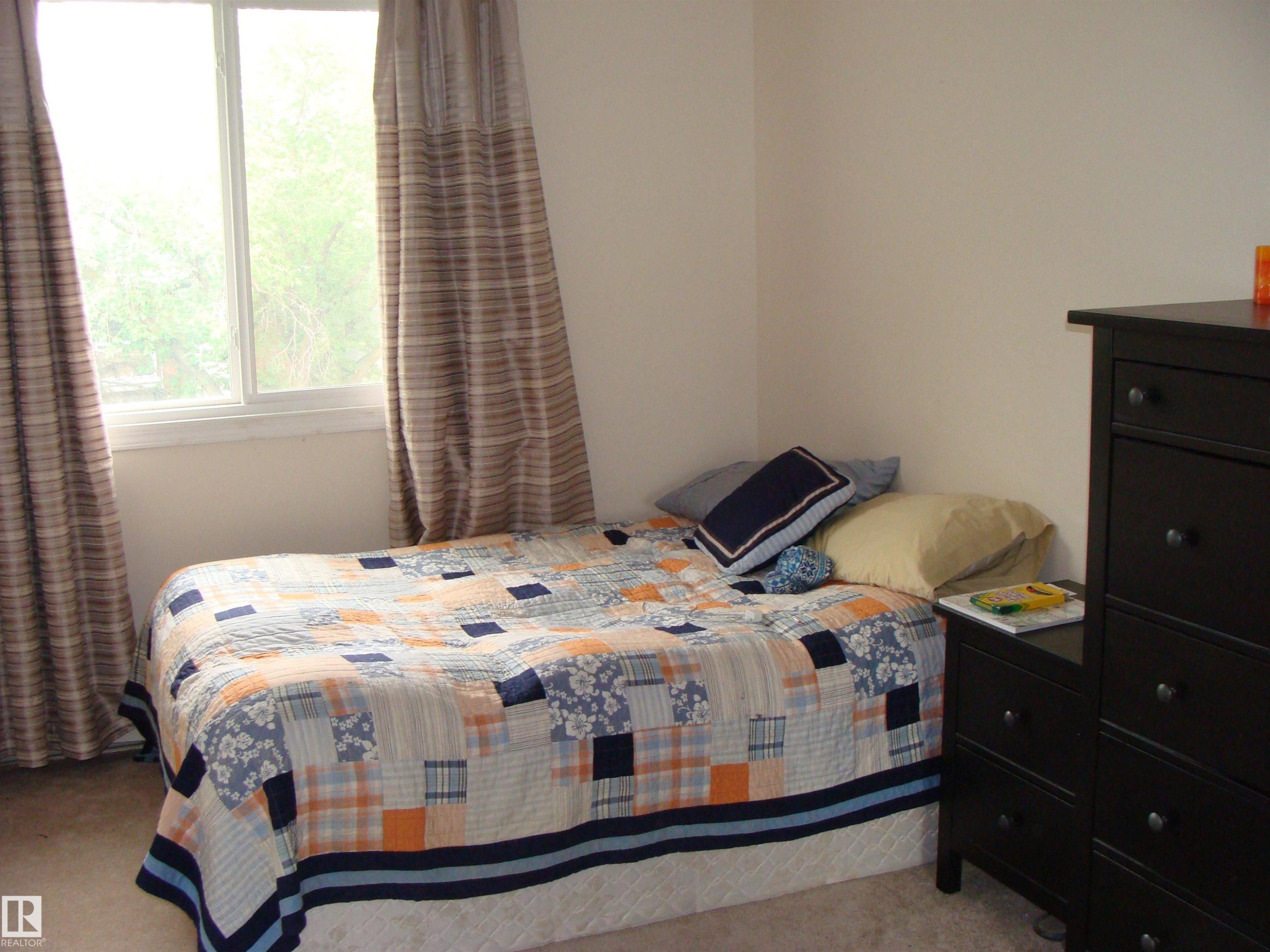 Bedroom featuring a window with white trim, carpeting, and light-toned walls - #401 10326 117 St Nw, Edmonton, AB - Indoor Photo Showing Bedroom