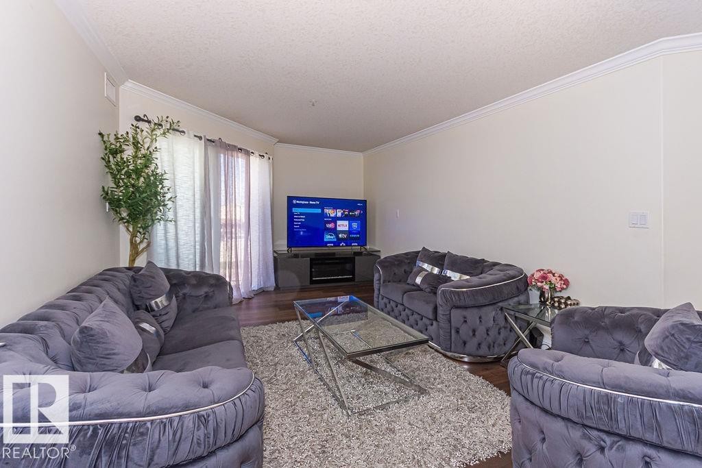 Spacious living area featuring wood-finish flooring, light-toned walls, and crown molding - 214 13005 140 Avenue, Edmonton, AB - Indoor Photo Showing Living Room