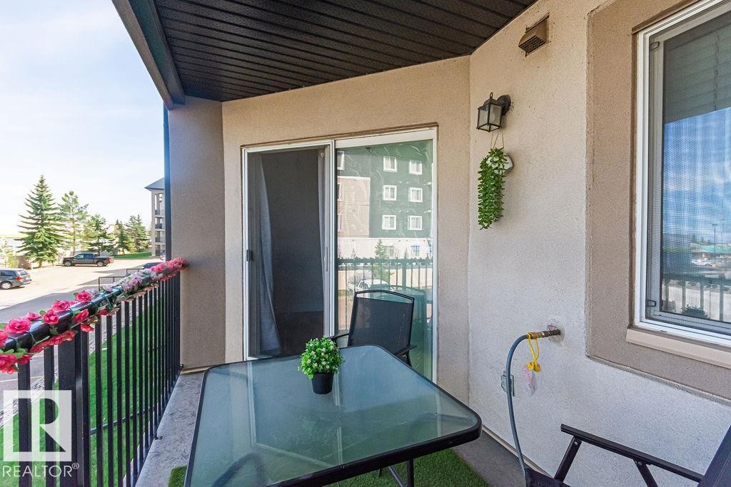 Private balcony featuring a black metal railing, stucco exterior, and a sliding glass door with screen - 214 13005 140 Avenue, Edmonton, AB - Outdoor With Exterior