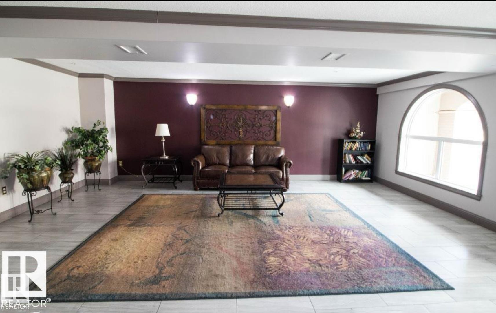 Spacious interior featuring light-toned tile flooring, a prominent arched window, and a built-in bookshelf - 214 13005 140 Avenue, Edmonton, AB - Indoor