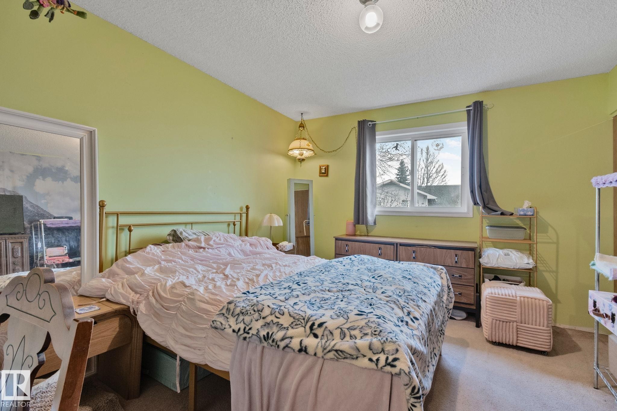 Spacious bedroom featuring light green walls, a large window, a ceiling-mounted light fixture, and textured carpeting - 4707 10A Avenue, Edmonton, AB - Indoor Photo Showing Bedroom