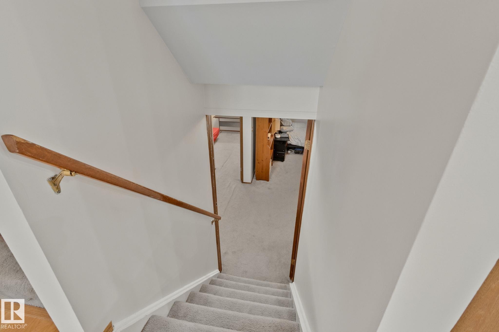 Carpeted staircase with light-colored walls and a wood handrail - 4707 10A Avenue, Edmonton, AB - Indoor Photo Showing Other Room