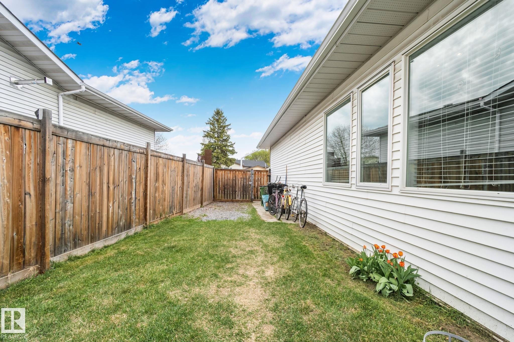 Fenced backyard featuring a gravel path, mature wooden fencing, manicured lawn, and white vinyl siding - 4707 10A Avenue, Edmonton, AB - Outdoor With Exterior