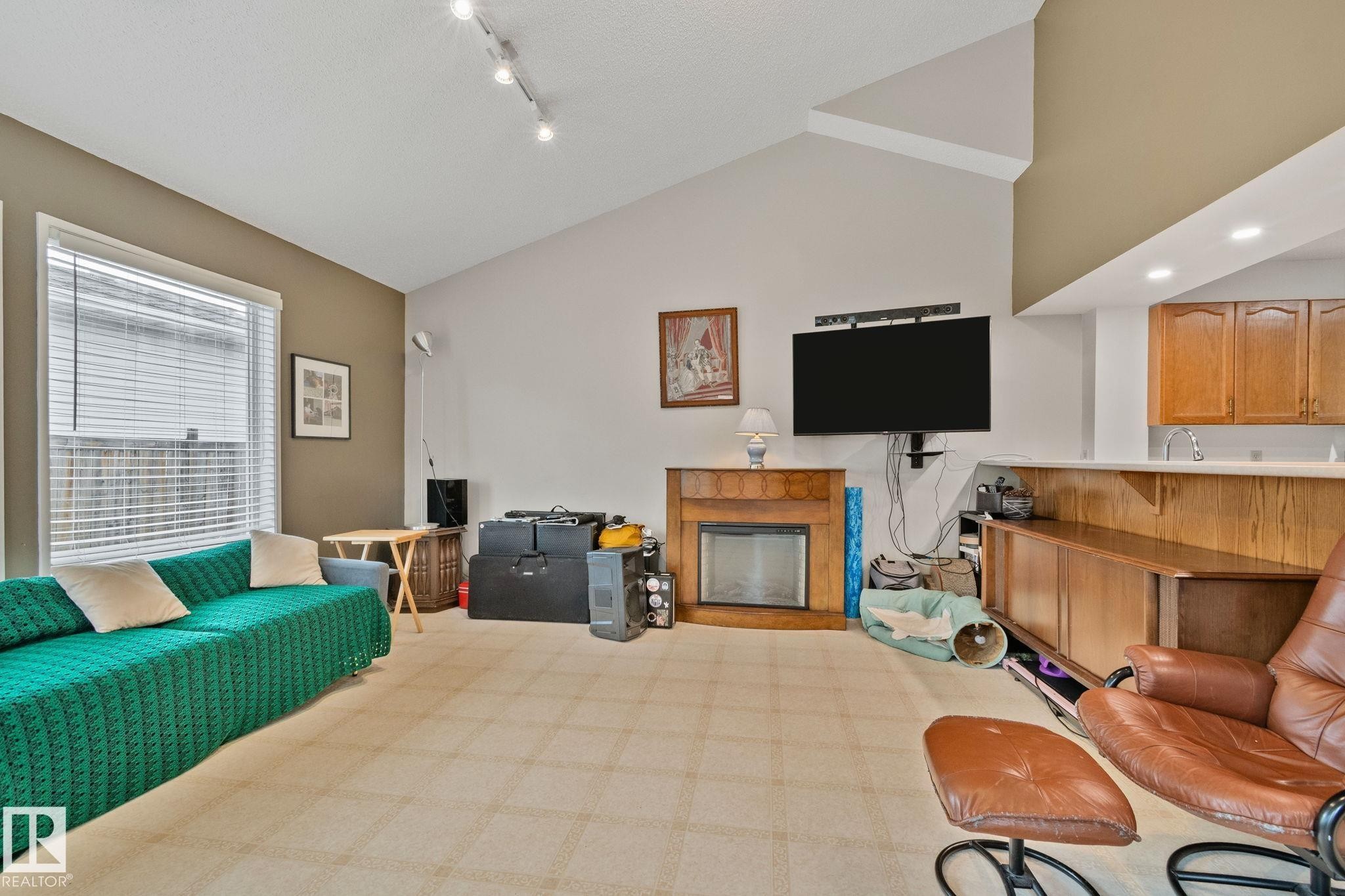 Living area featuring a vaulted ceiling, track lighting, and a corner fireplace with a wood surround - 4707 10A Avenue, Edmonton, AB - Indoor With Fireplace
