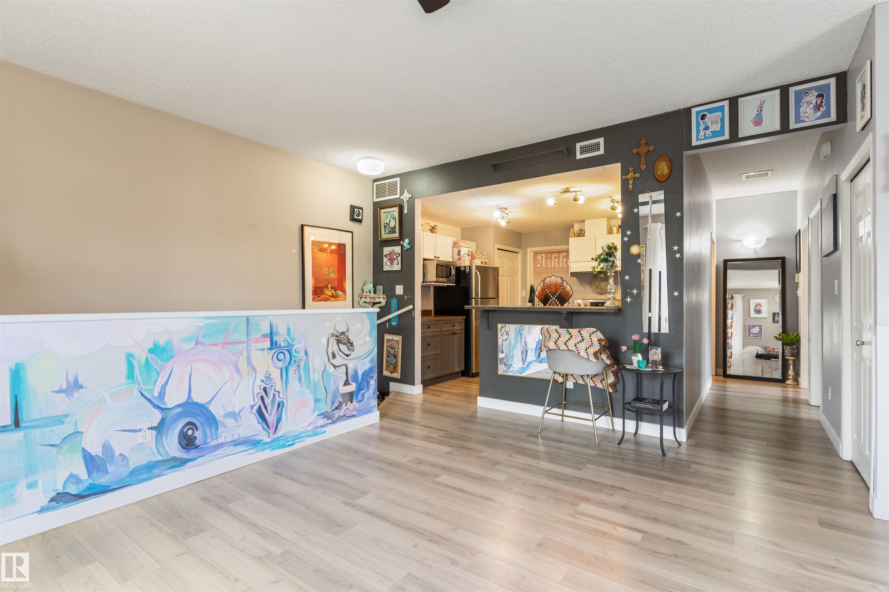 Open-concept living space featuring light wood-finish flooring, a contemporary partition wall with an artistic mural, a pass-through kitchen with a breakfast bar, and recessed lighting - 73 3040 Spence Wynd, Edmonton, AB - Indoor Photo Showing Other Room