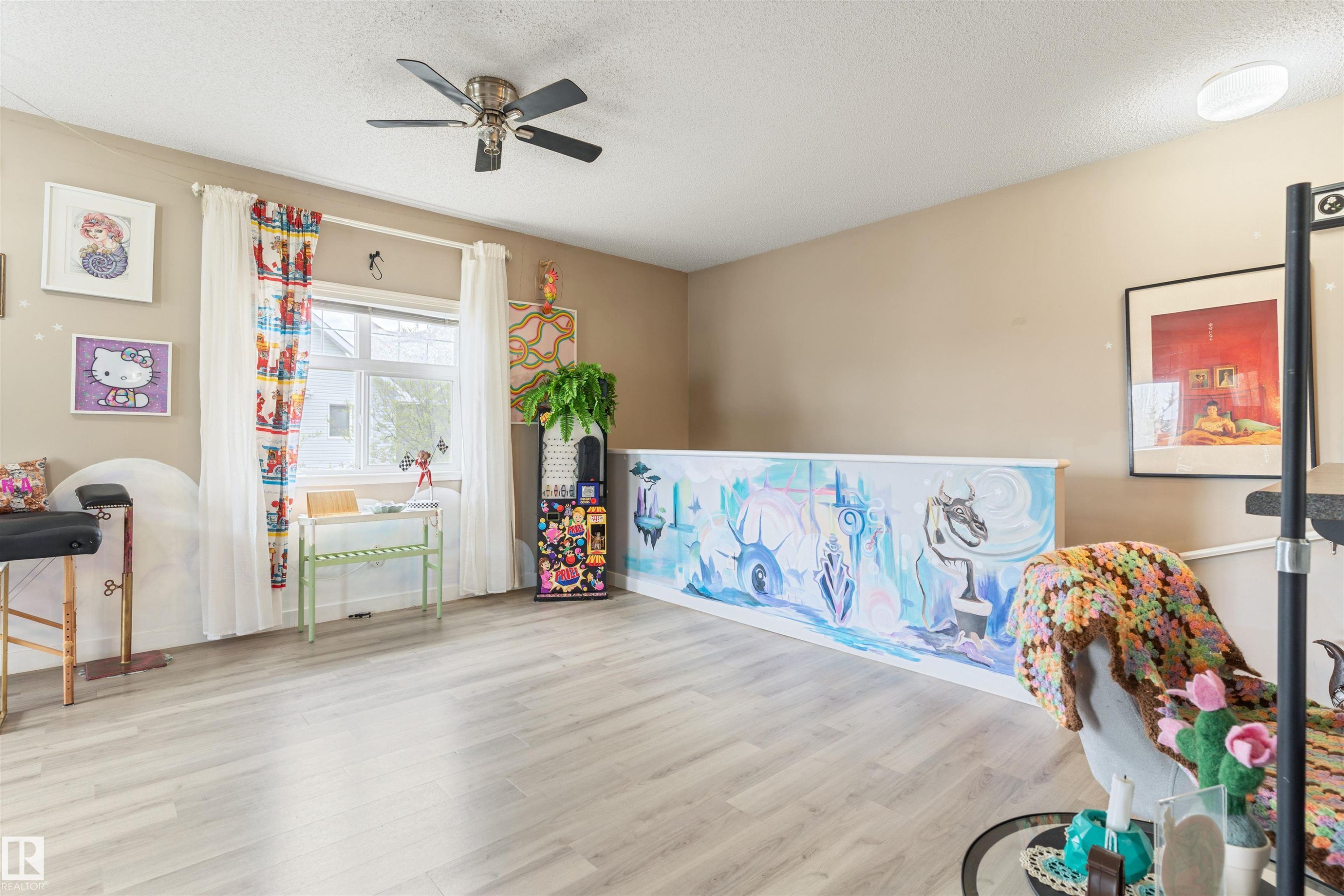 Spacious room featuring light wood-finish flooring, a ceiling fan, and a large window with white curtains - 73 3040 Spence Wynd, Edmonton, AB - Indoor Photo Showing Other Room