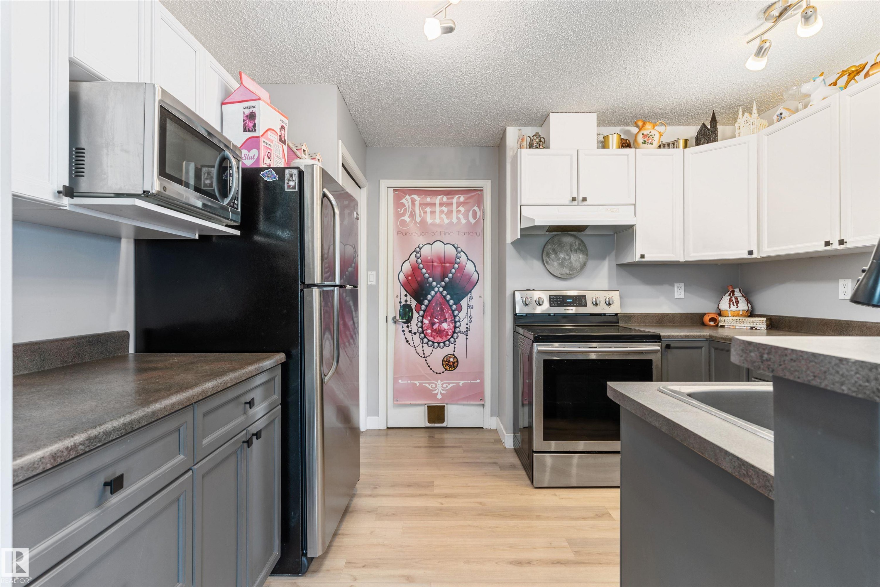 Kitchen featuring wood-finish flooring, stainless steel appliances, white upper cabinetry, and contrasting gray lower cabinetry - 73 3040 Spence Wynd, Edmonton, AB - Indoor Photo Showing Kitchen With Stainless Steel Kitchen