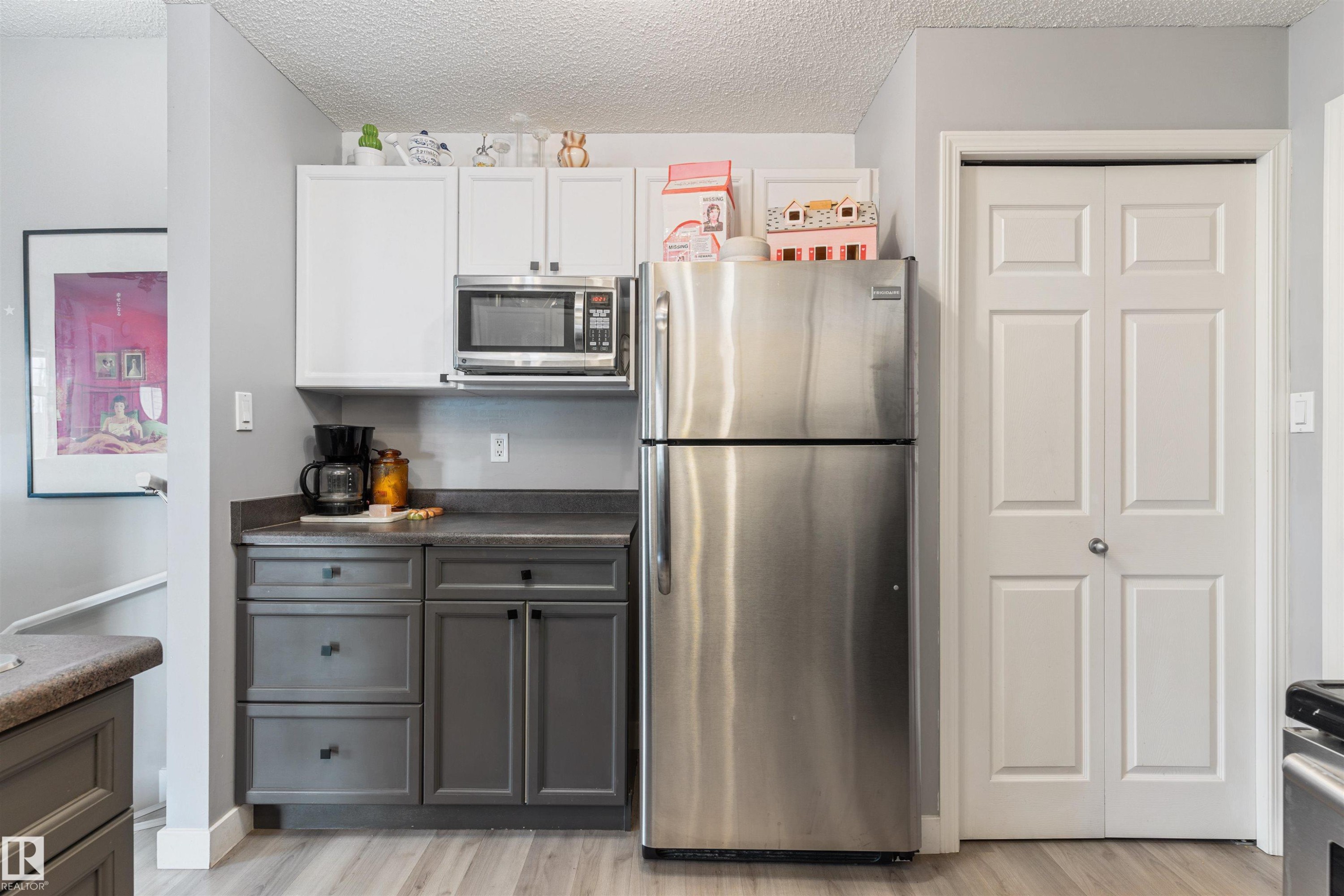Kitchen area featuring stainless steel appliances, two-tone cabinetry with white upper and gray lower cabinets, dark countertop, and wood-finish flooring - 73 3040 Spence Wynd, Edmonton, AB - Indoor Photo Showing Kitchen With Stainless Steel Kitchen