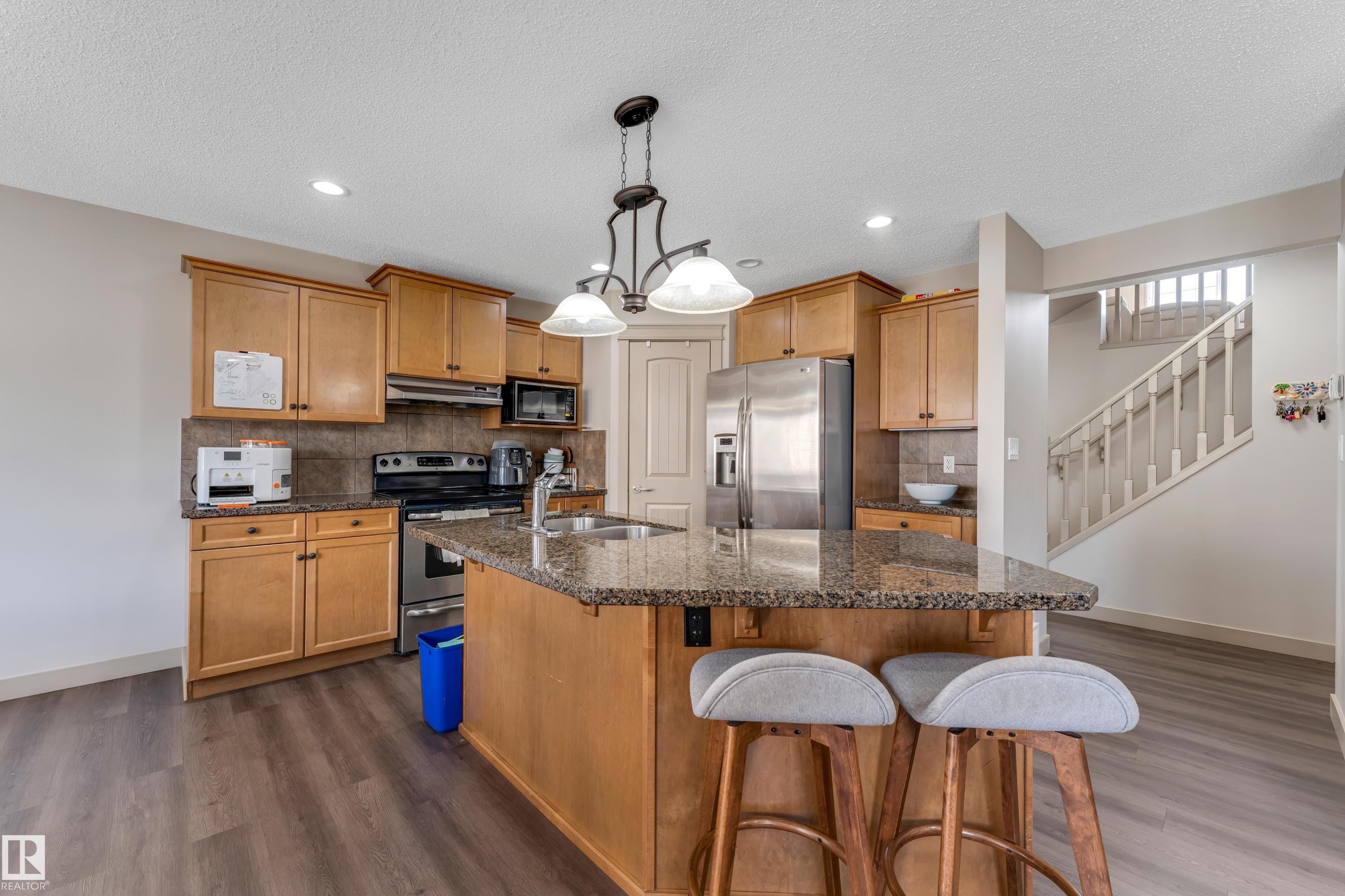 Well-appointed kitchen featuring wood cabinetry, stainless steel appliances, and a central island with a granite countertop and integrated sink - 463 Tamarack Green, Edmonton, AB - Indoor Photo Showing Kitchen With Double Sink