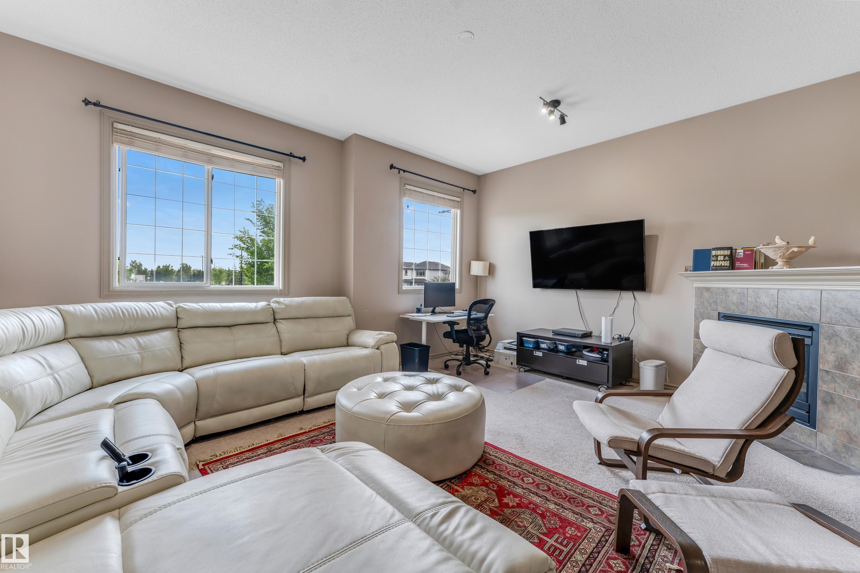 This inviting living area features neutral-toned walls, windows providing natural light, and a fireplace with a tiled surround - 463 Tamarack Green, Edmonton, AB - Indoor Photo Showing Living Room With Fireplace