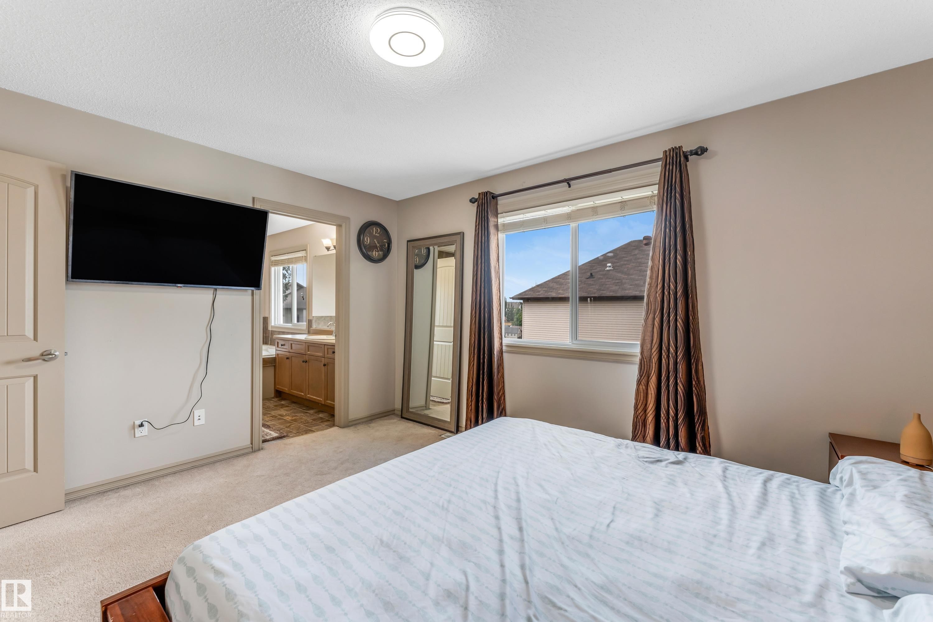 The property features a bedroom with light-colored carpeting, a window dressed with dark-patterned curtains, and light-colored walls - 463 Tamarack Green, Edmonton, AB - Indoor Photo Showing Bedroom
