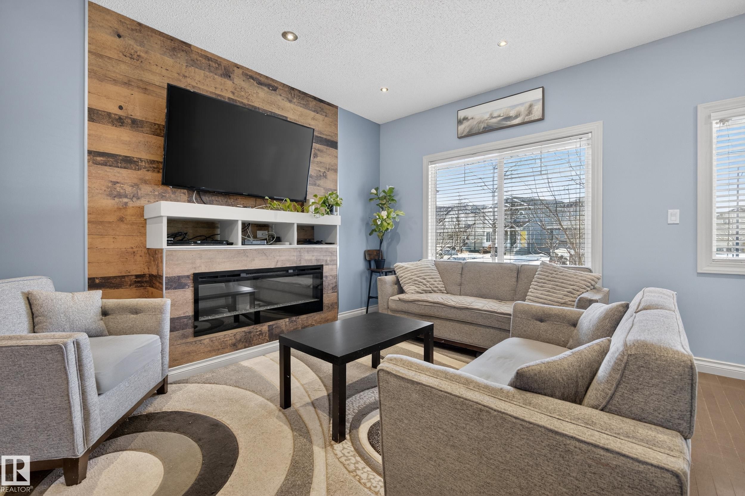 Living area featuring a floor-to-ceiling wood-panel accent wall, integrated electric fireplace, and recessed lighting - 7074 Cardinal Way, Edmonton, AB - Indoor Photo Showing Living Room With Fireplace