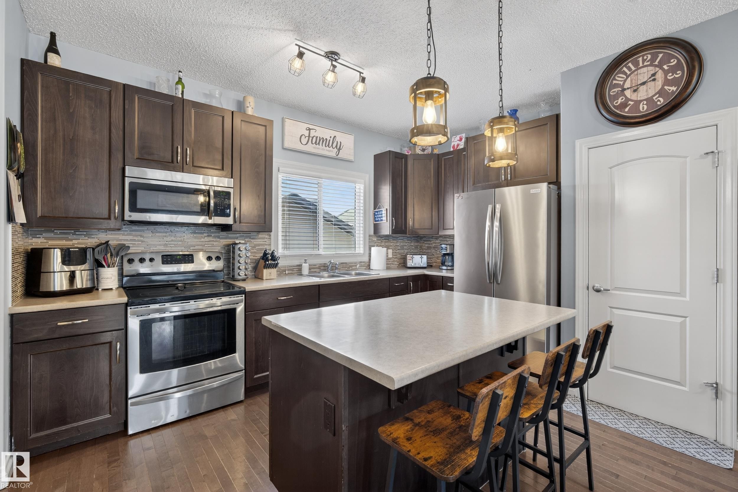Kitchen featuring dark wood-finish cabinetry, stainless steel appliances, a center island with countertop seating, and wood-finish flooring - 7074 Cardinal Way, Edmonton, AB - Indoor Photo Showing Kitchen