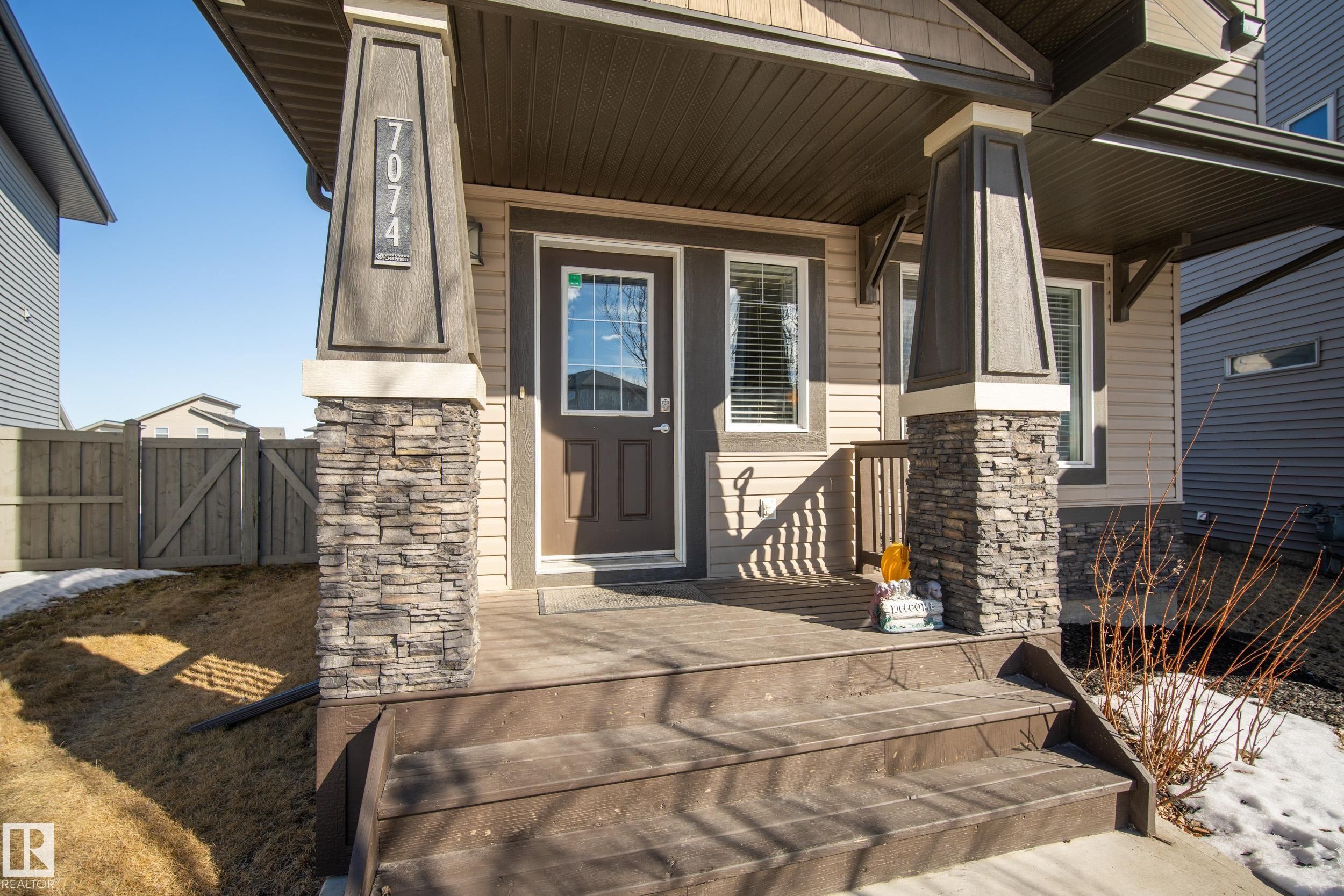 Inviting front entrance featuring a covered porch, stone-clad columns, durable siding, and a wooden fence - 7074 Cardinal Way, Edmonton, AB - Outdoor With Deck Patio Veranda