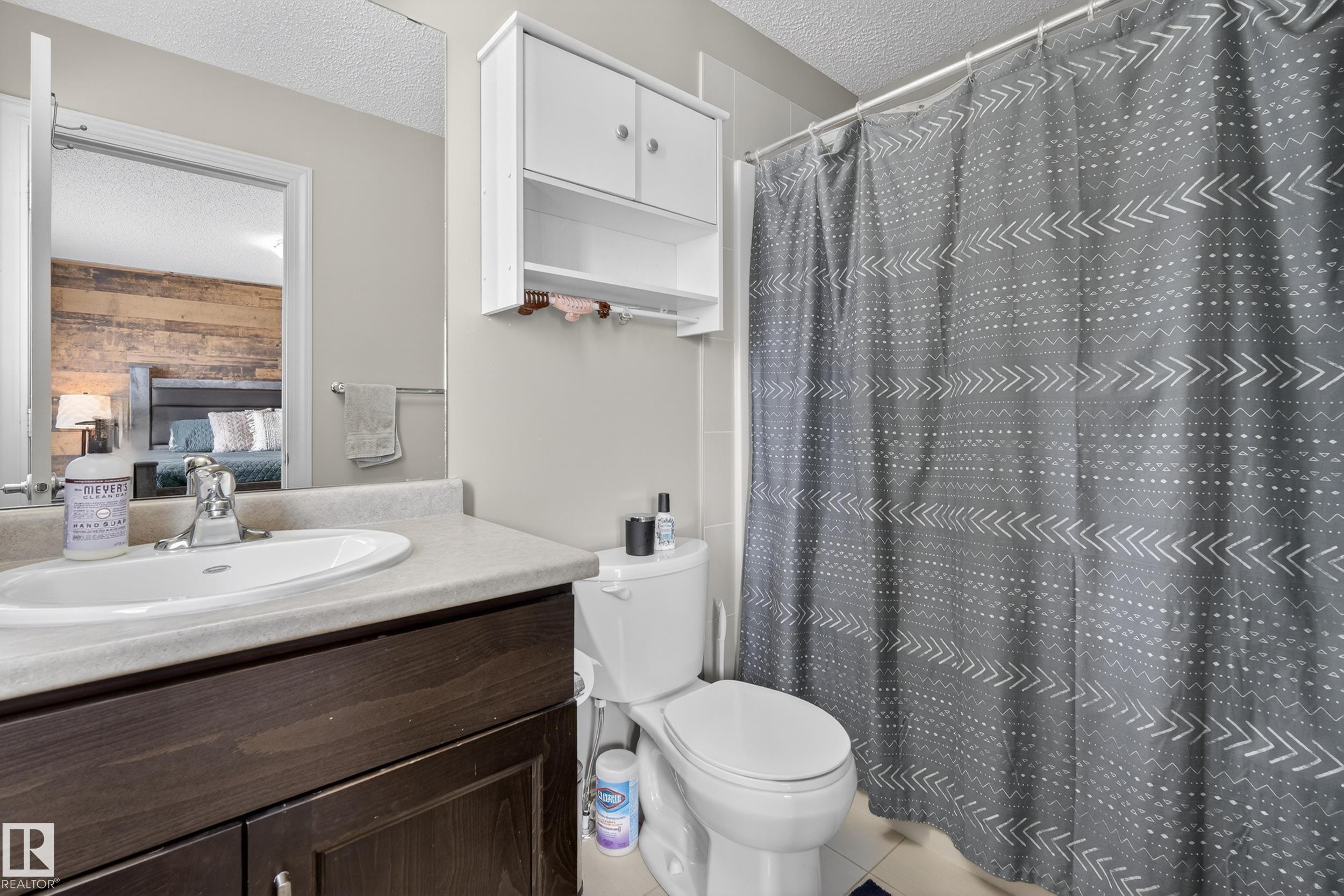 Bathroom featuring a vanity with an integrated sink, dark wood-finish cabinetry, white wall-mounted storage, a toilet, and a tiled shower area - 7074 Cardinal Way, Edmonton, AB - Indoor Photo Showing Bathroom