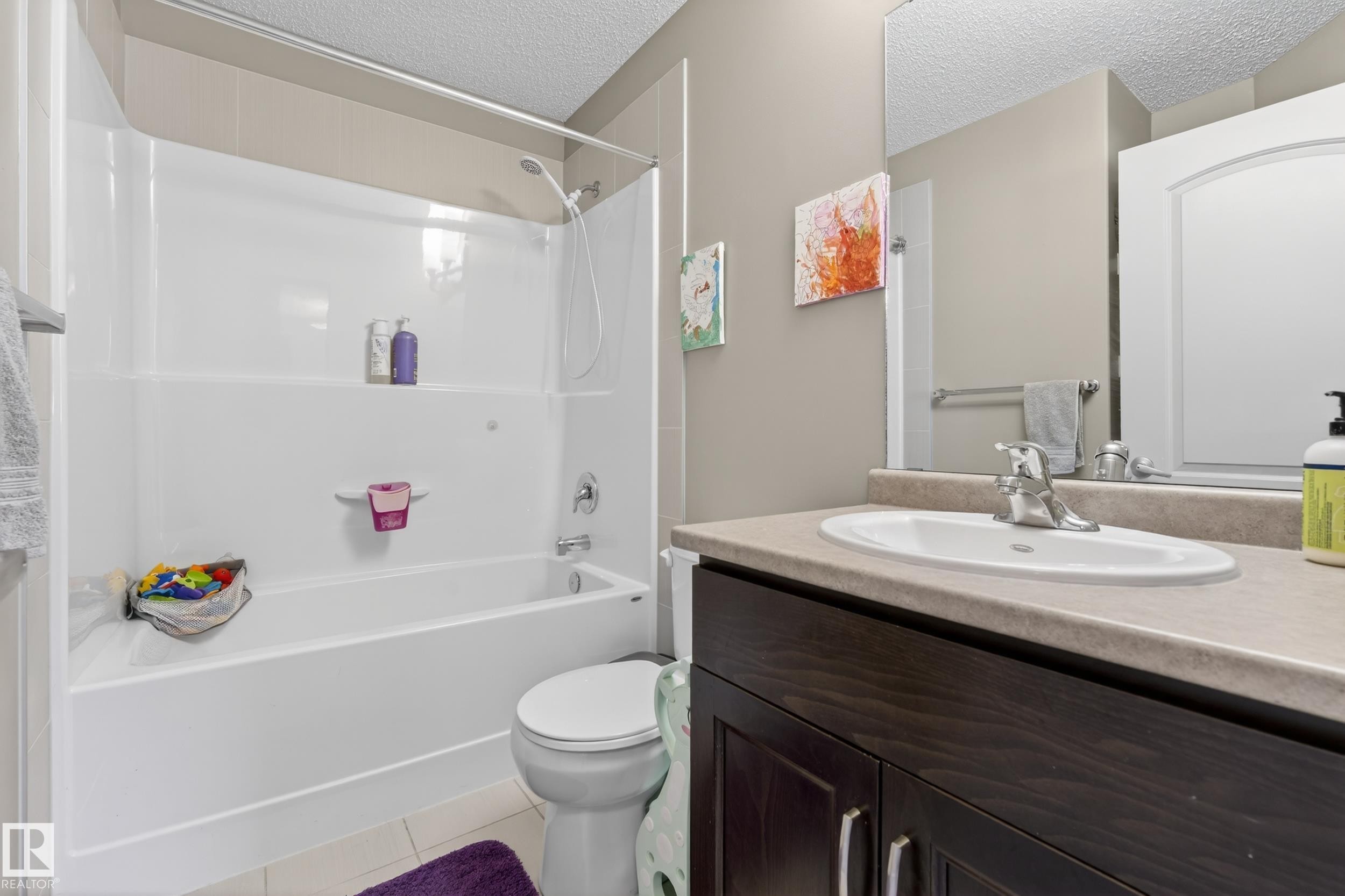 Bathroom featuring a white tub-shower combination with a sliding glass door, a dark wood-finish vanity with a light-toned countertop, and an oval undermount sink with a chrome faucet - 7074 Cardinal Way, Edmonton, AB - Indoor Photo Showing Bathroom