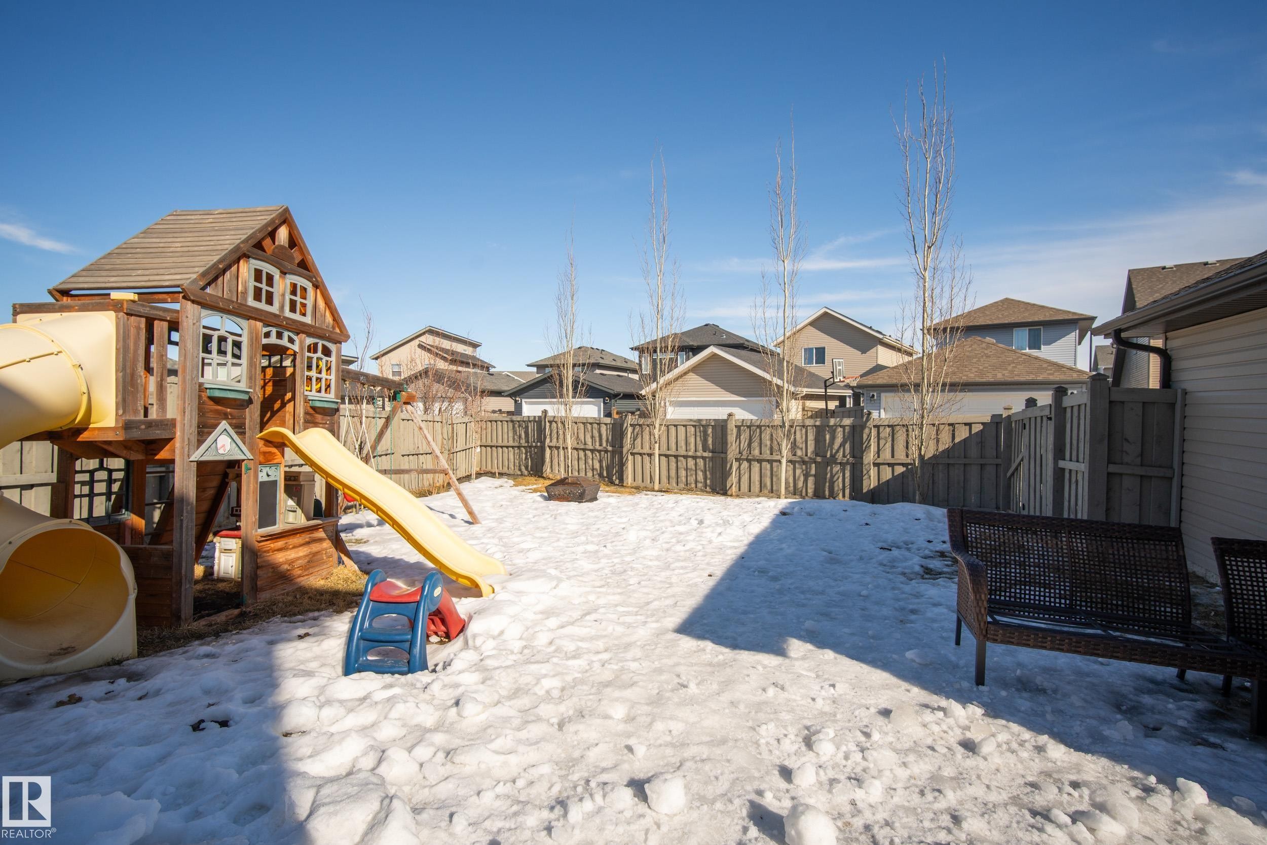 Fully fenced backyard featuring a wooden privacy fence, mature trees, and a clear blue sky - 7074 Cardinal Way, Edmonton, AB - Outdoor