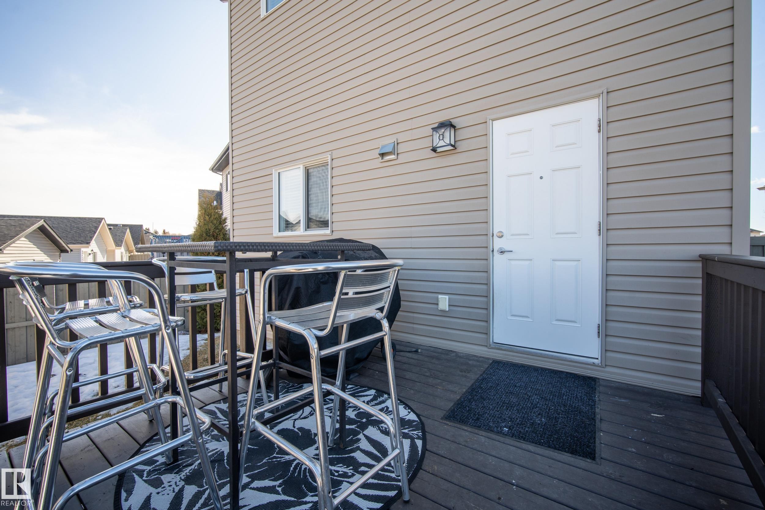 Exterior deck with composite decking, featuring a privacy railing, decorative outdoor lighting, and a white paneled entry door - 7074 Cardinal Way, Edmonton, AB - Outdoor With Exterior
