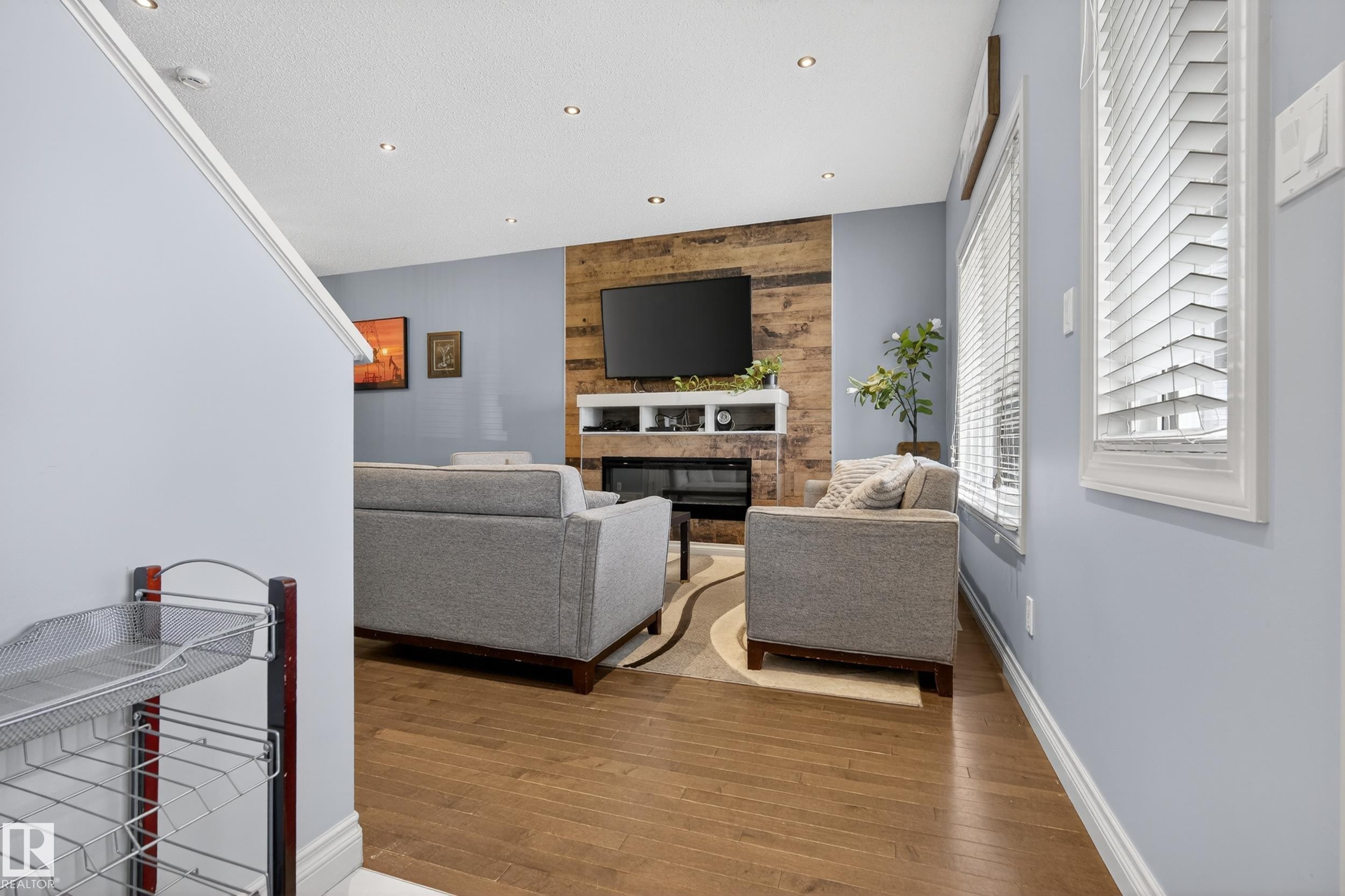 Living area featuring wood-finish flooring, recessed lighting, and a prominent wood-paneled accent wall with a built-in fireplace - 7074 Cardinal Way, Edmonton, AB - Indoor With Fireplace
