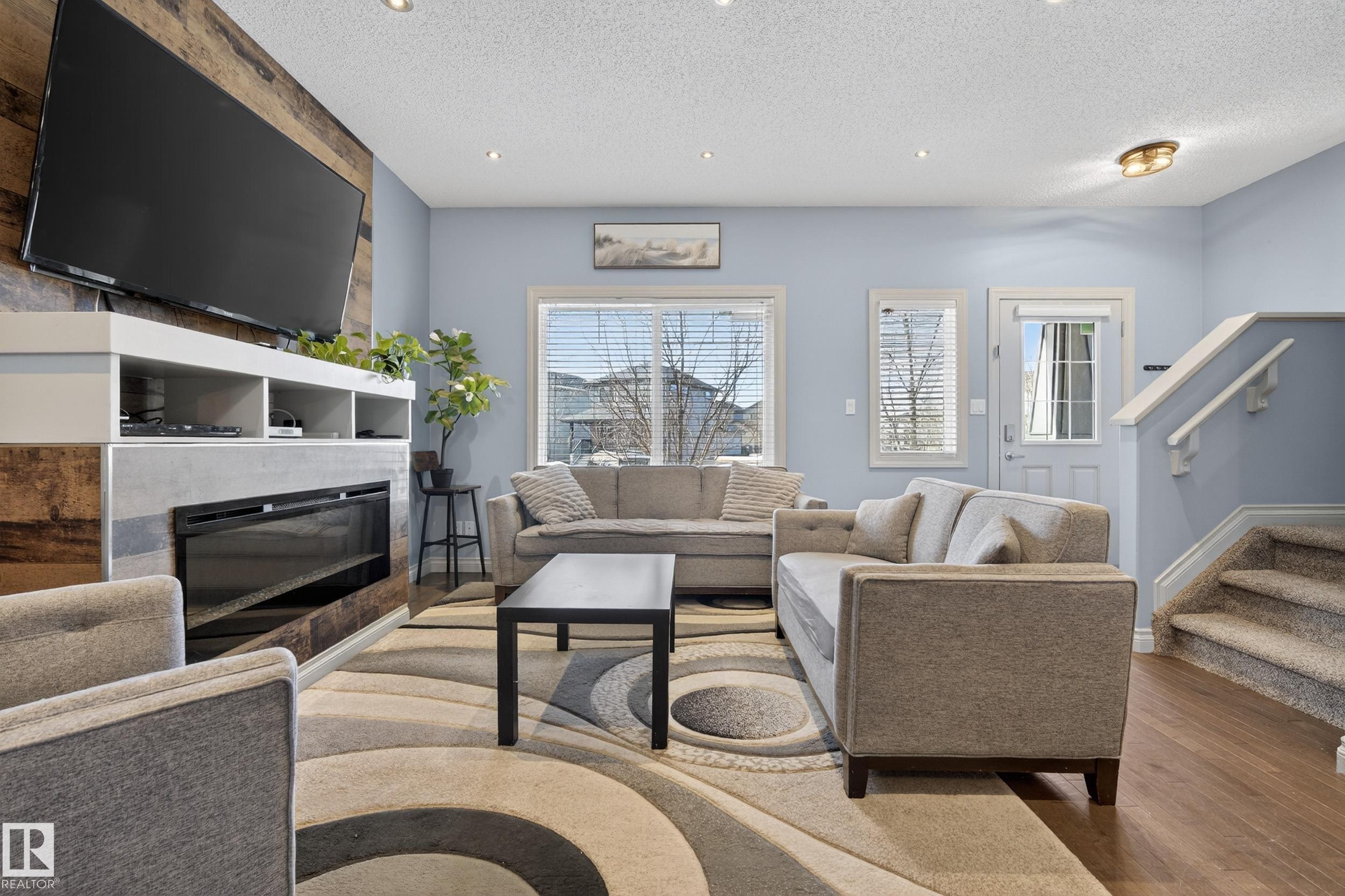 Living area featuring a modern fireplace with a wood-finish accent wall, built-in media shelving, and recessed lighting - 7074 Cardinal Way, Edmonton, AB - Indoor Photo Showing Living Room With Fireplace