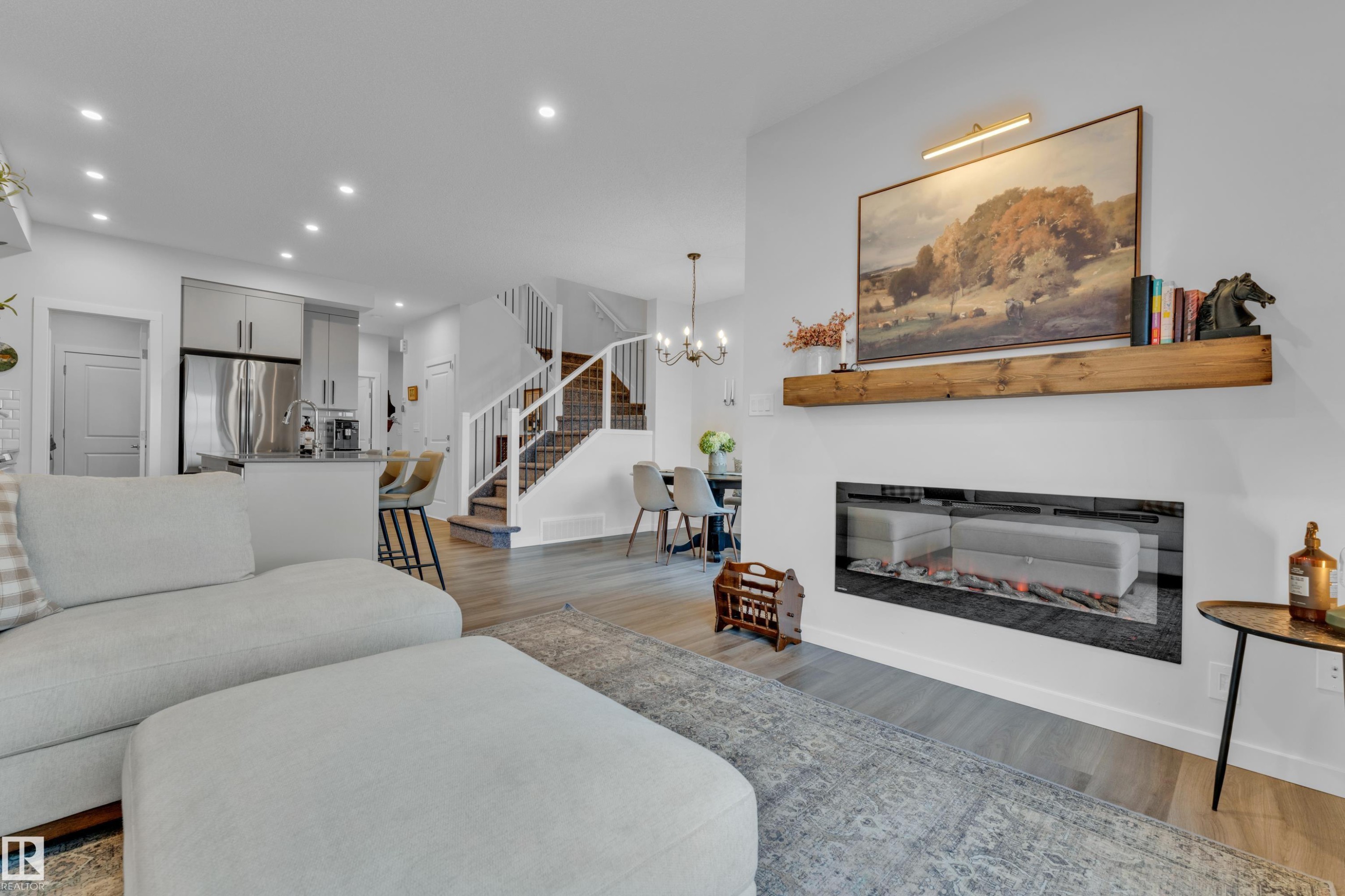 Spacious living area featuring an inset linear fireplace with a wood-finish mantel and a light wood-finish flooring - 17319 2 St Nw, Edmonton, AB - Indoor Photo Showing Living Room With Fireplace