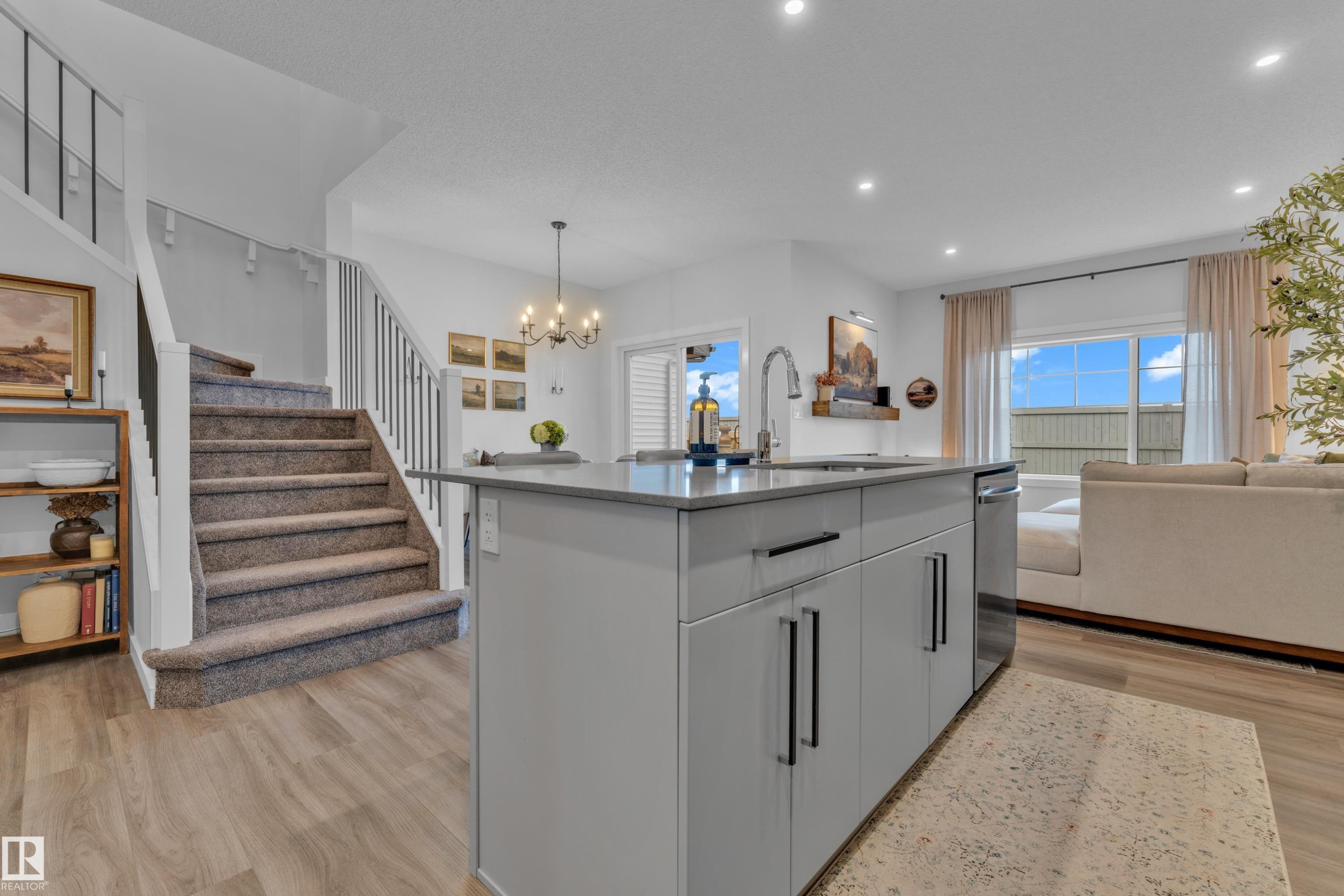 Kitchen island featuring a stainless steel sink with a high-arc faucet, light gray cabinetry with black hardware, and a light-toned countertop - 17319 2 St Nw, Edmonton, AB - Indoor Photo Showing Kitchen