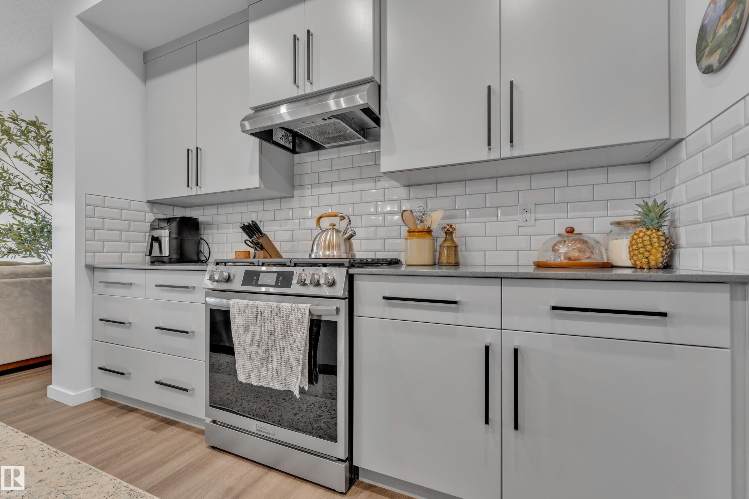 Modern kitchen featuring light gray cabinetry with black bar pulls, a stainless steel range and hood, white subway tile backsplash, dark countertops, and wood-finish flooring - 17319 2 St Nw, Edmonton, AB - Indoor Photo Showing Kitchen With Upgraded Kitchen