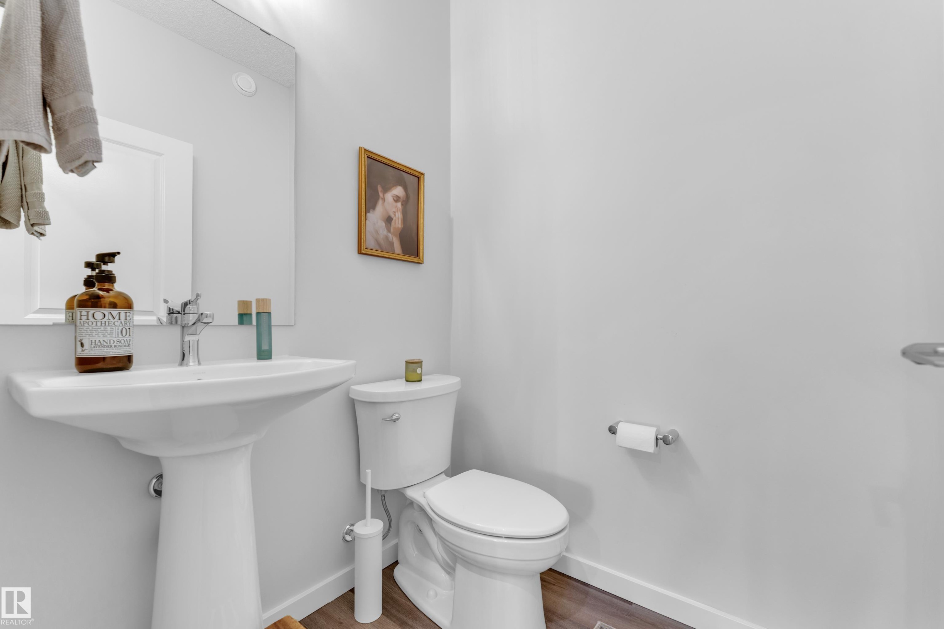Pedestal sink with chrome faucet, a white toilet, and wood-finish flooring - 17319 2 St Nw, Edmonton, AB - Indoor Photo Showing Bathroom