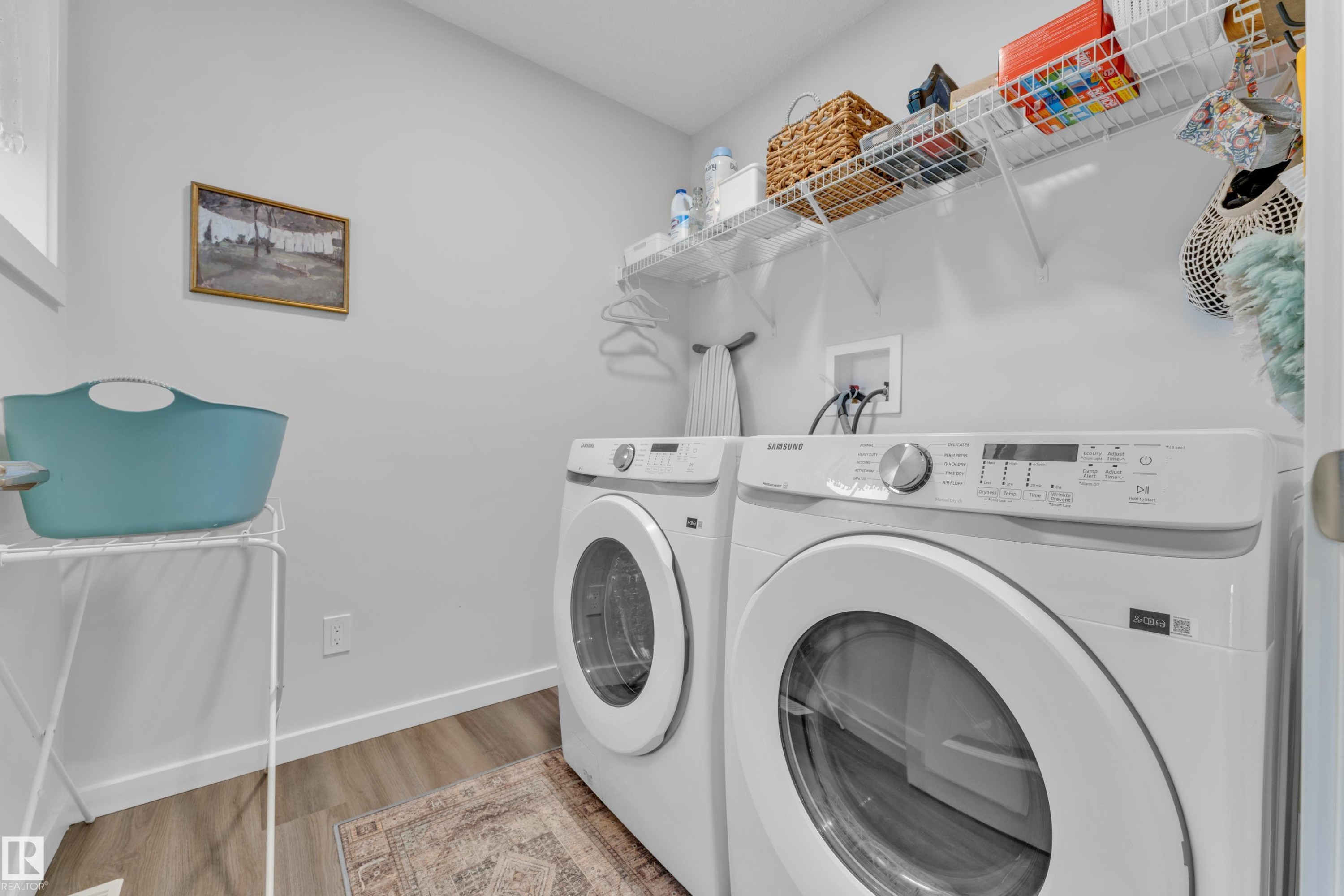 Dedicated laundry area featuring a front-loading washer and dryer, wood-finish flooring, and white wire shelving - 17319 2 St Nw, Edmonton, AB - Indoor Photo Showing Laundry Room