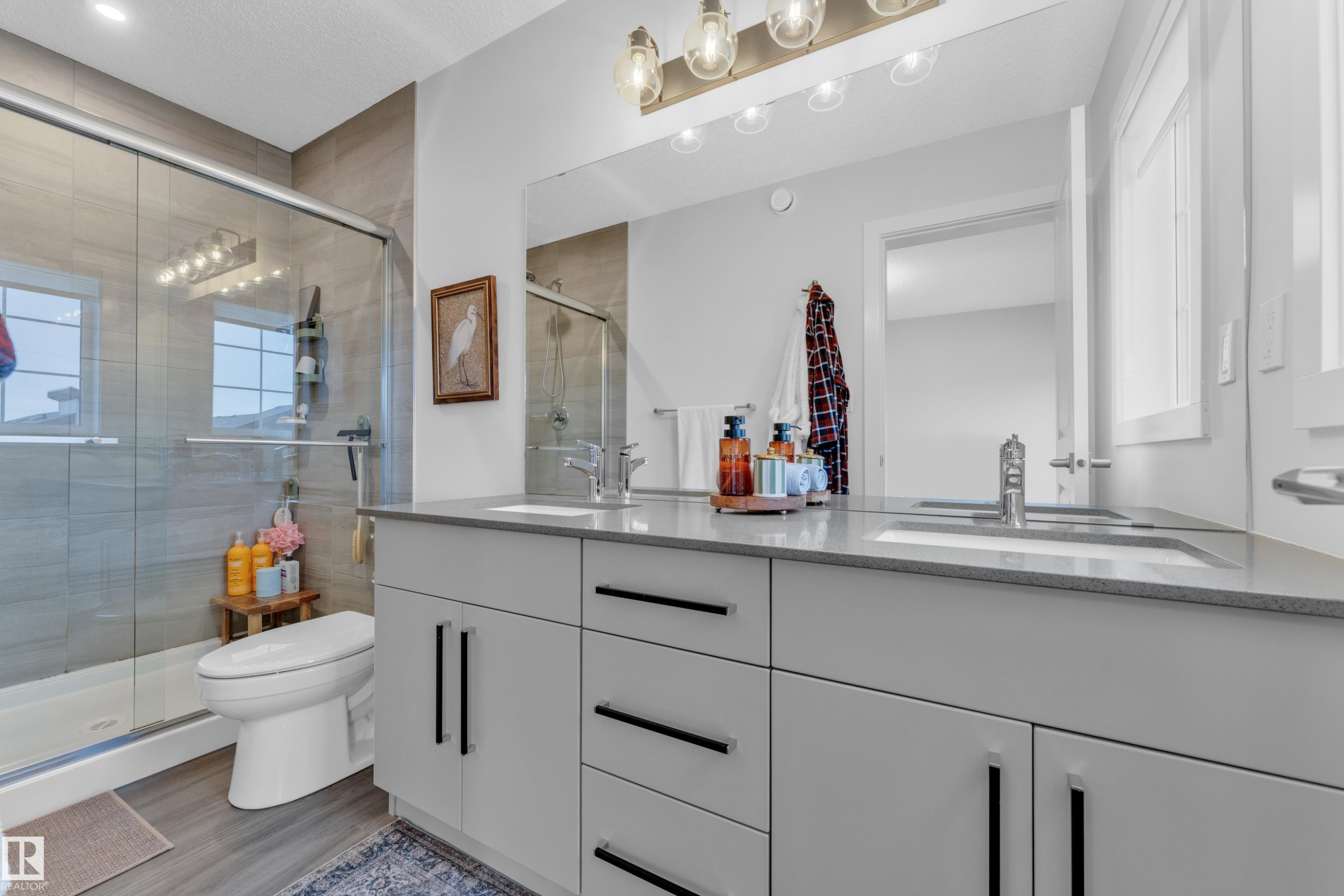 Dual vanity with light gray cabinetry and integrated sinks, complemented by a large mirror and multi-bulb light fixture - 17319 2 St Nw, Edmonton, AB - Indoor Photo Showing Bathroom