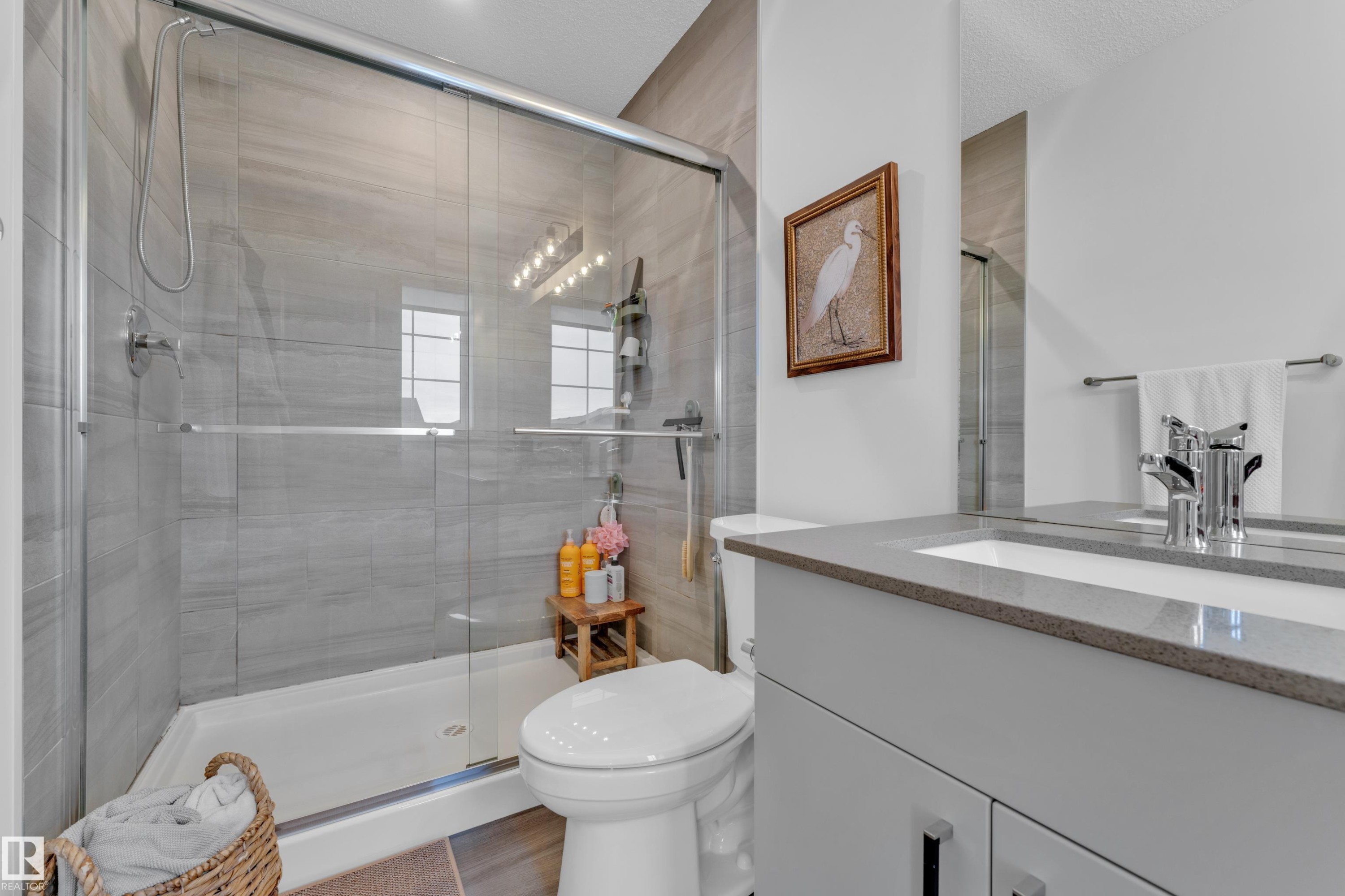 Contemporary bathroom featuring a spacious glass-enclosed shower with gray tiled walls and a polished chrome shower head, a large vanity with a rectangular undermount sink, a gray countertop, and a chrome faucet, and wood-finish flooring - 17319 2 St Nw, Edmonton, AB - Indoor Photo Showing Bathroom