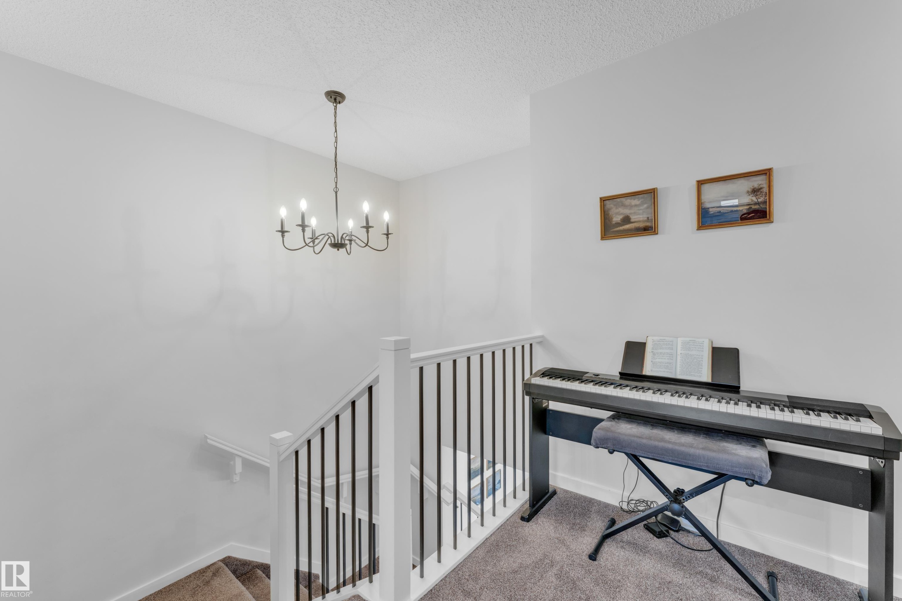 Staircase featuring white newel posts, black metal balusters, and a traditional chandelier - 17319 2 St Nw, Edmonton, AB - Indoor Photo Showing Other Room