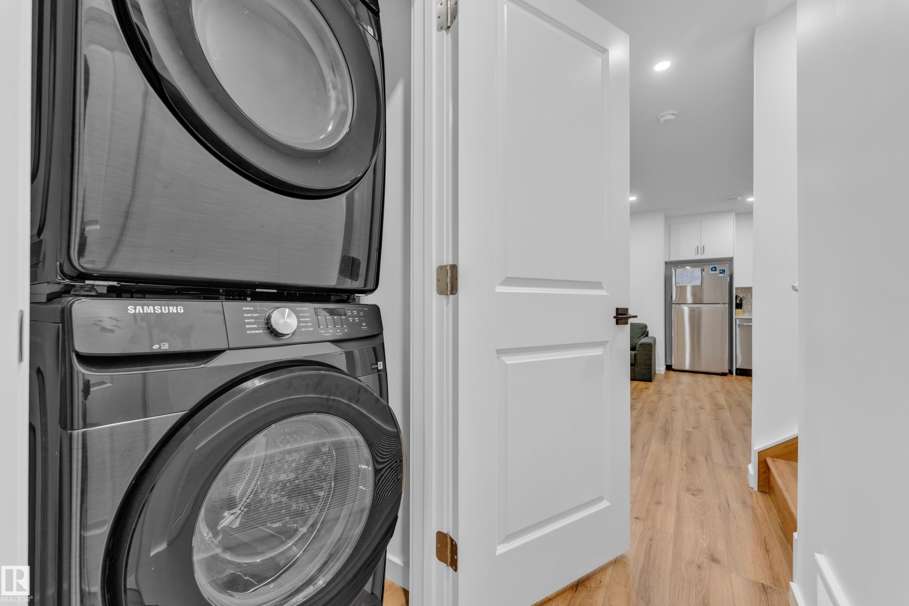 Stacked laundry appliances with a modern dark finish, recessed lighting, wood-finish flooring, and white interior doors - 17319 2 St Nw, Edmonton, AB - Indoor Photo Showing Laundry Room