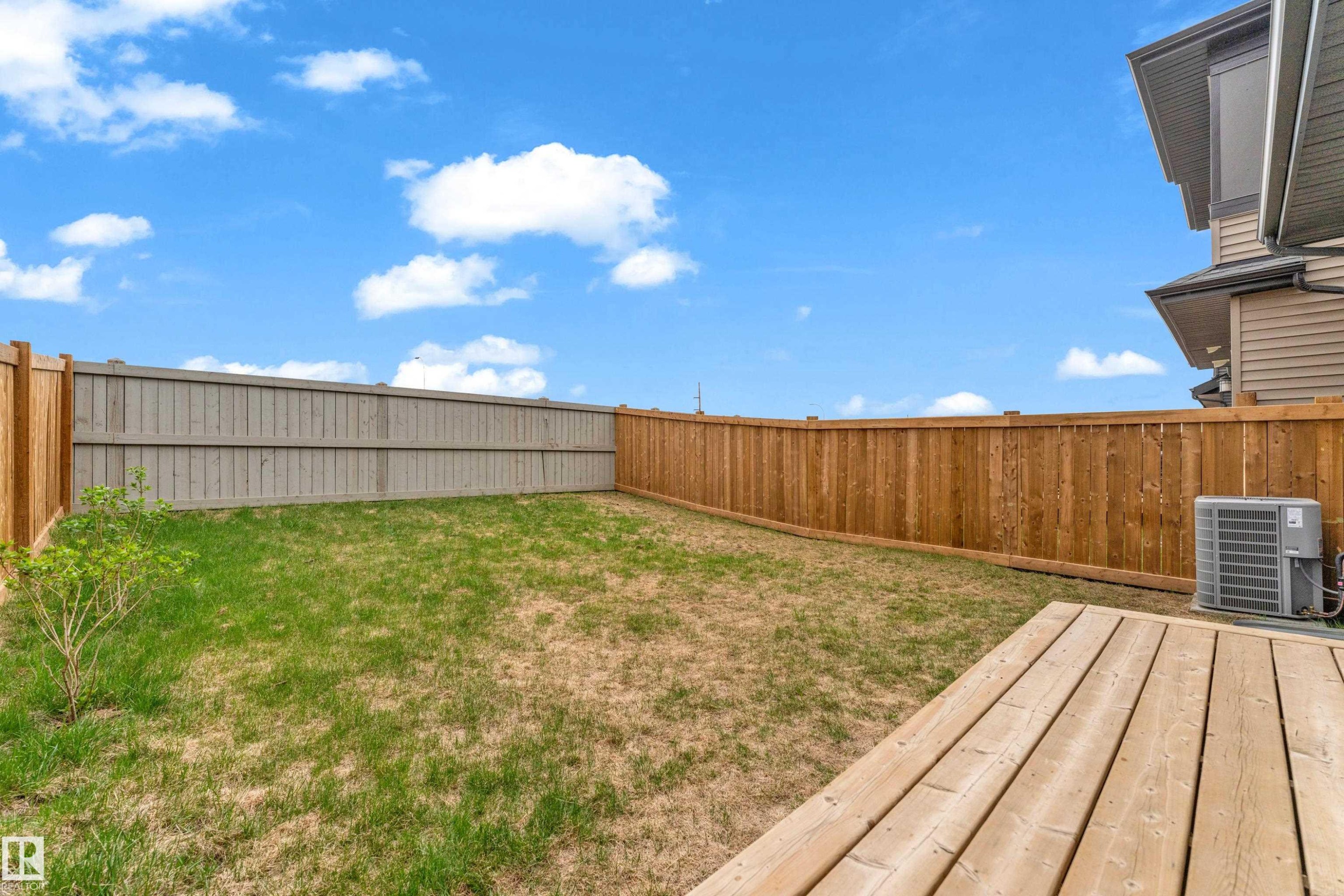 Expansive backyard featuring a natural wood deck, varied wood fencing, and a grassy area - 17319 2 St Nw, Edmonton, AB - Outdoor