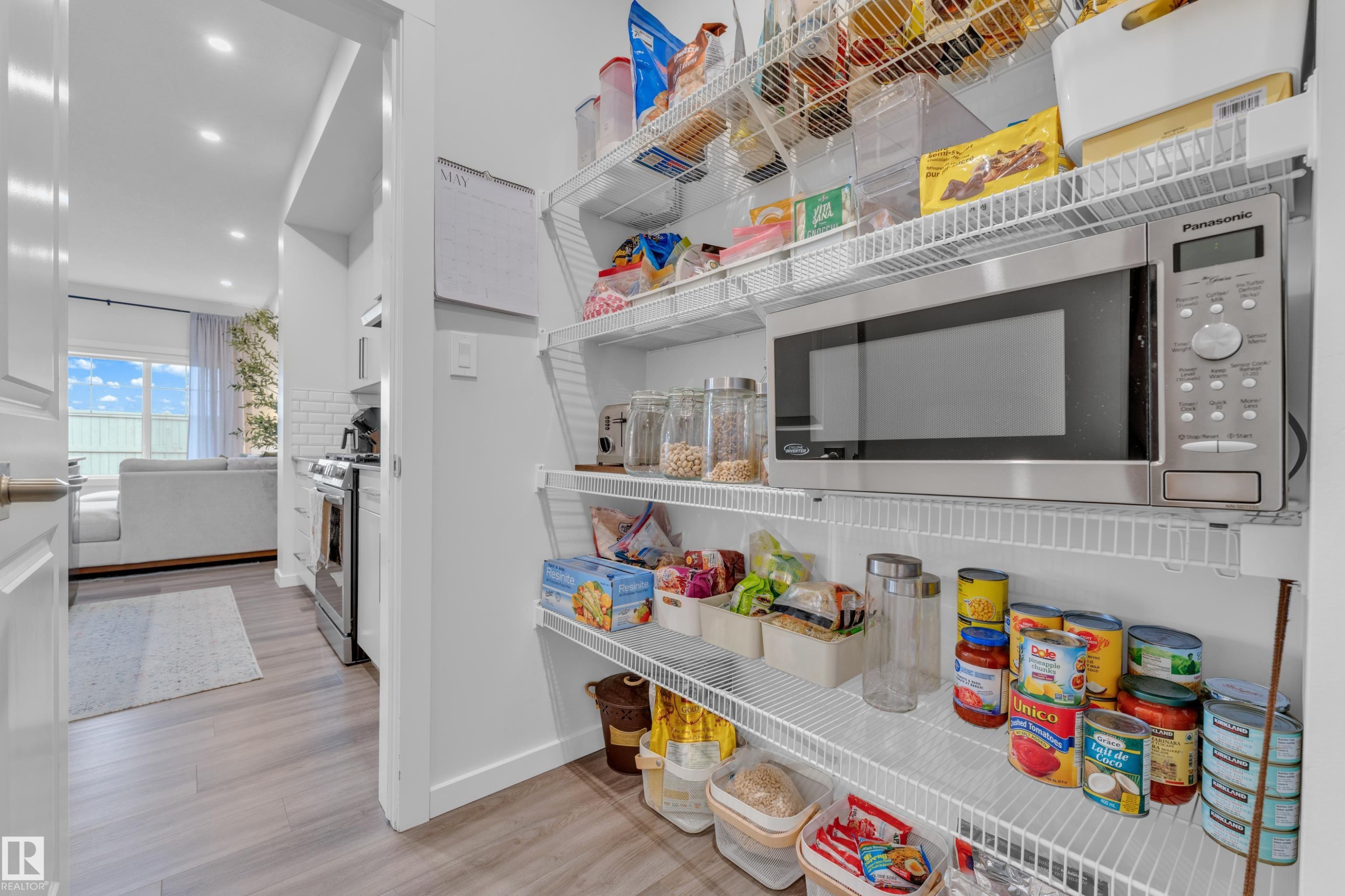 Spacious pantry with wire shelving, integrated microwave, and wood-finish flooring - 17319 2 St Nw, Edmonton, AB - Indoor Photo Showing Other Room