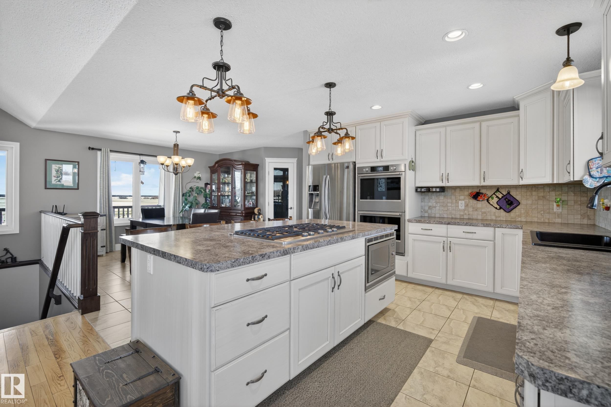 The kitchen features white cabinetry, integrated double ovens, and a central island with a cooktop and seating for four - 531064 Range Road 174, Rural Lamont County, AB - Indoor Photo Showing Kitchen