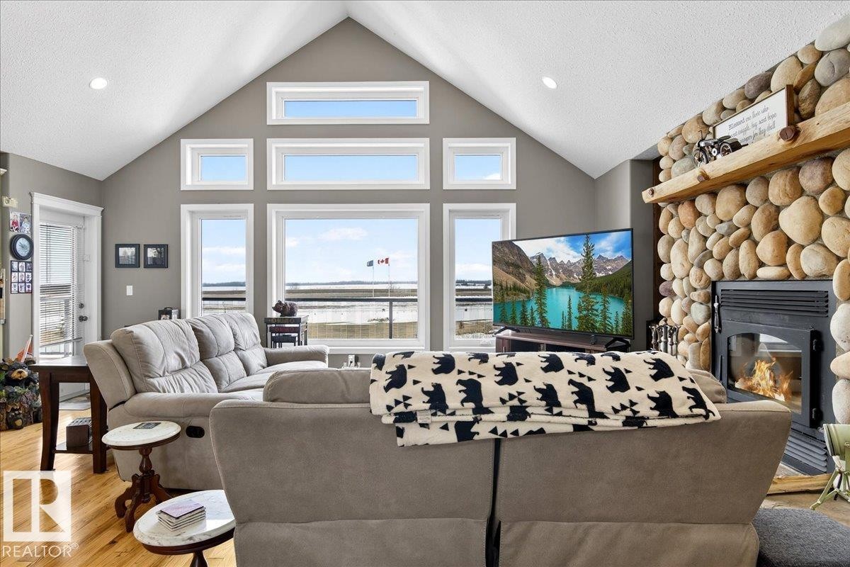 This living space features prominent windows, a stone-clad fireplace with a timber mantel, and light-toned hardwood flooring - 531064 Range Road 174, Rural Lamont County, AB - Indoor Photo Showing Living Room With Fireplace