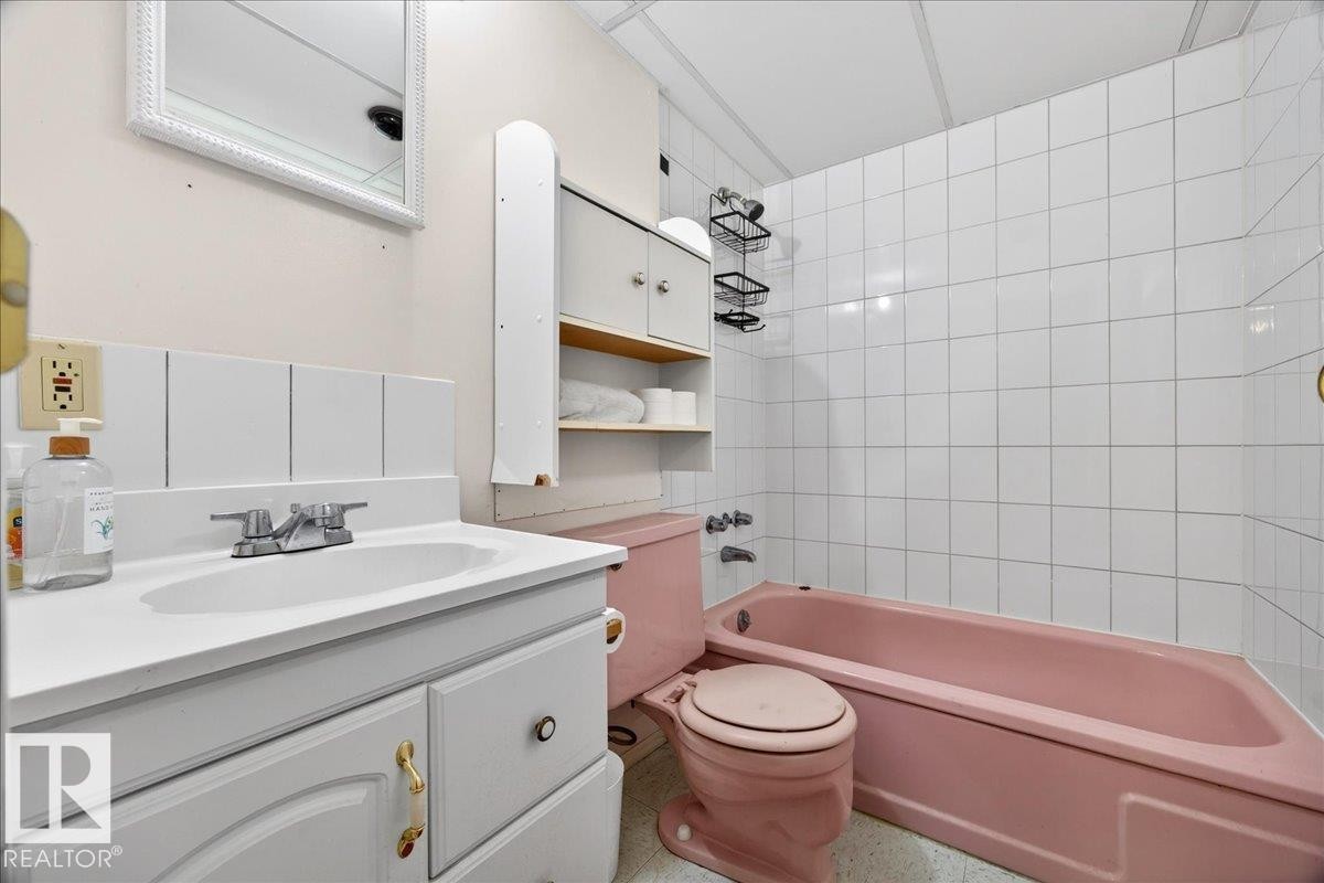Bathroom featuring a white vanity with integrated sink, white tiled backsplash, pink bathtub, and pink toilet - 4212 105 Avenue, Edmonton, AB - Indoor Photo Showing Bathroom