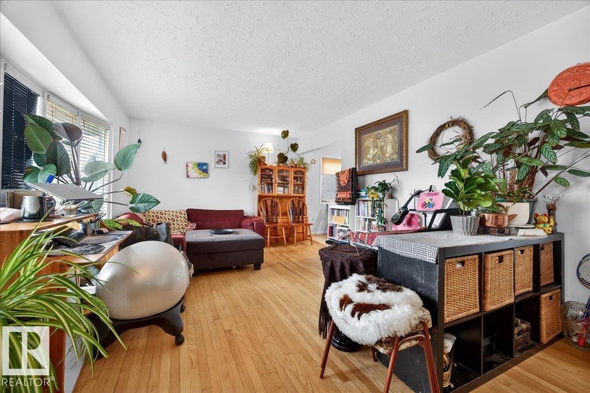 Spacious living area featuring wood-finish flooring, white walls, and a large window with horizontal blinds - 4212 105 Avenue, Edmonton, AB - Indoor Photo Showing Living Room