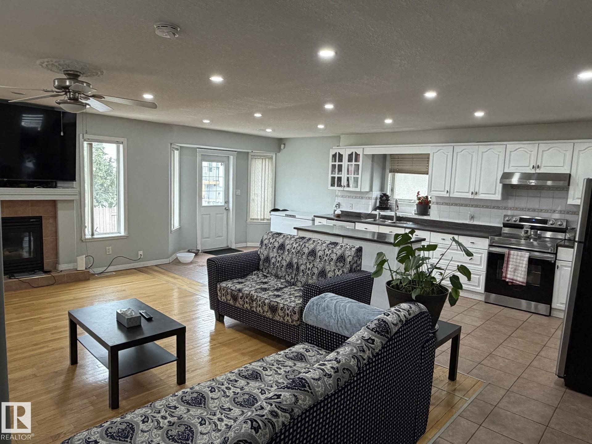 Open-concept living area featuring a kitchen with white cabinetry and stainless steel appliances - 3139 34B Avenue, Edmonton, AB - Indoor Photo Showing Living Room With Fireplace