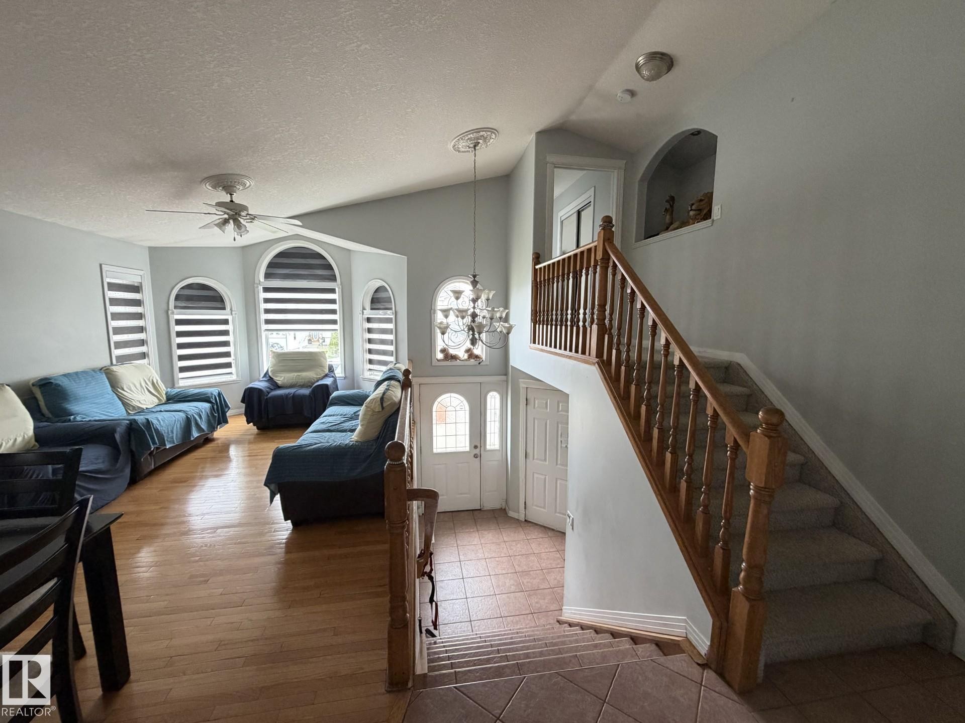 Foyer and living area featuring a decorative chandelier, arched window accents, wood-finish flooring, a ceiling fan, and a wood banister staircase with carpeted steps - 3139 34B Avenue, Edmonton, AB - Indoor