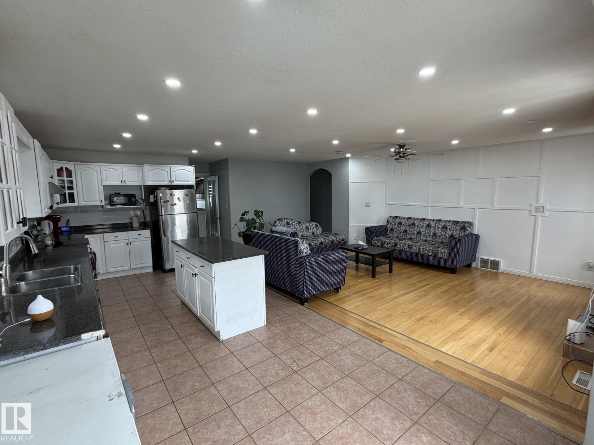 Open-concept living space featuring a kitchen with white cabinetry and dark countertops, a central island, and stainless steel appliances - 3139 34B Avenue, Edmonton, AB - Indoor