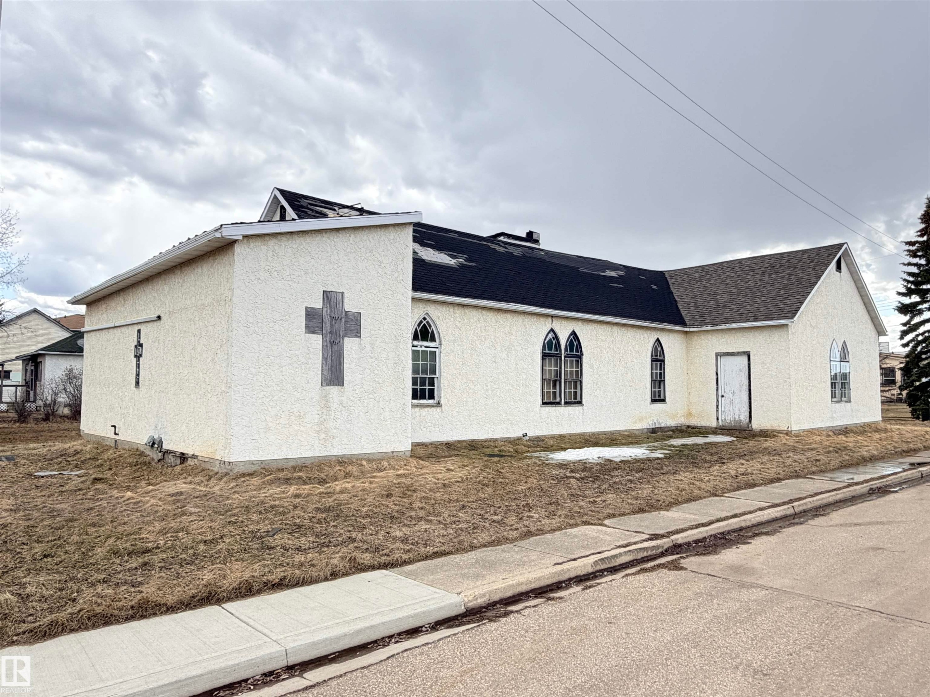 Stucco-clad structure featuring a multi-pitch shingle roof and multiple arched windows - 5036 49 Street, Clyde, AB - Outdoor With Exterior