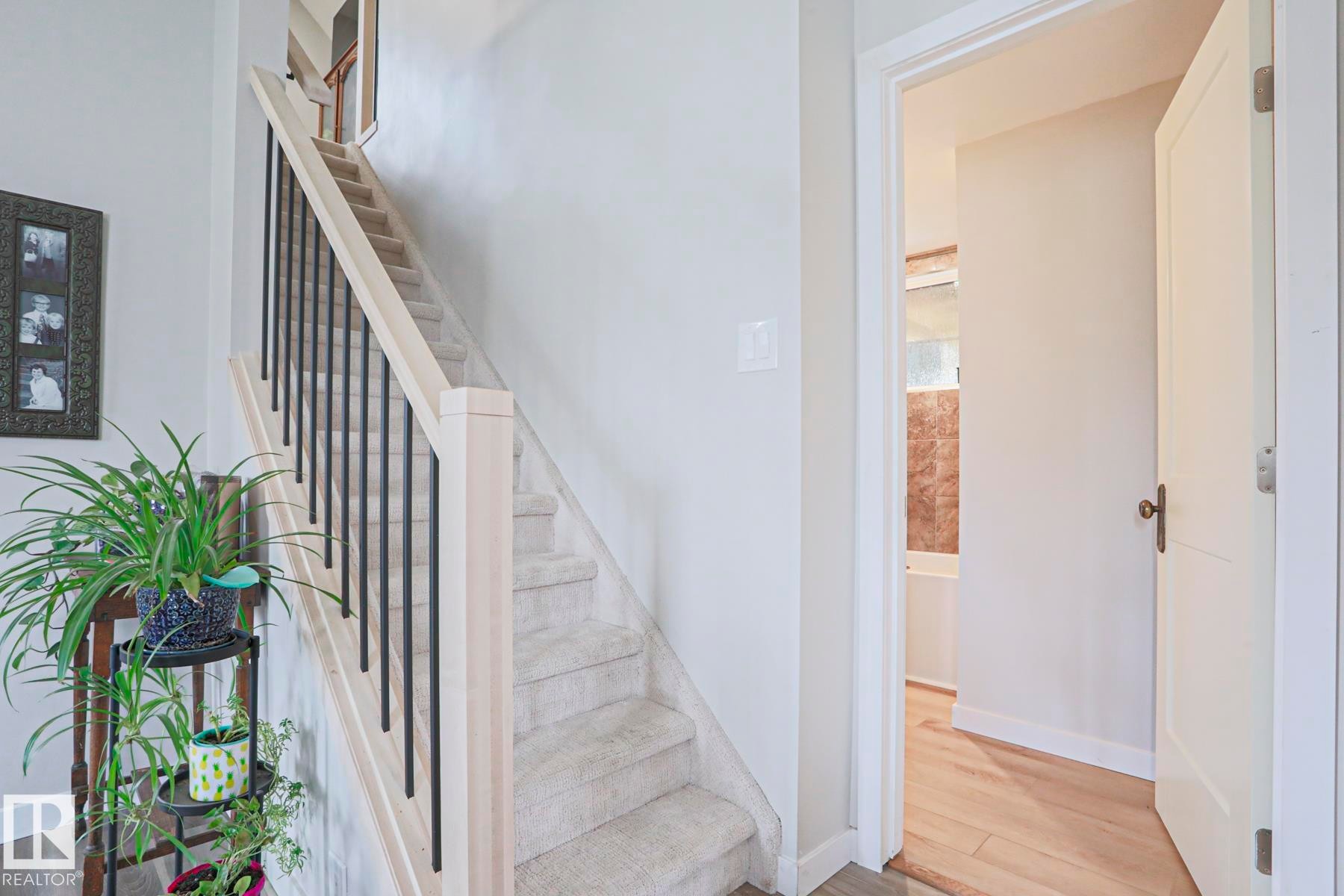 Carpeted staircase with light wood newel posts and black metal balusters - 5113 53 Avenue, Stony Plain, AB - Indoor Photo Showing Other Room