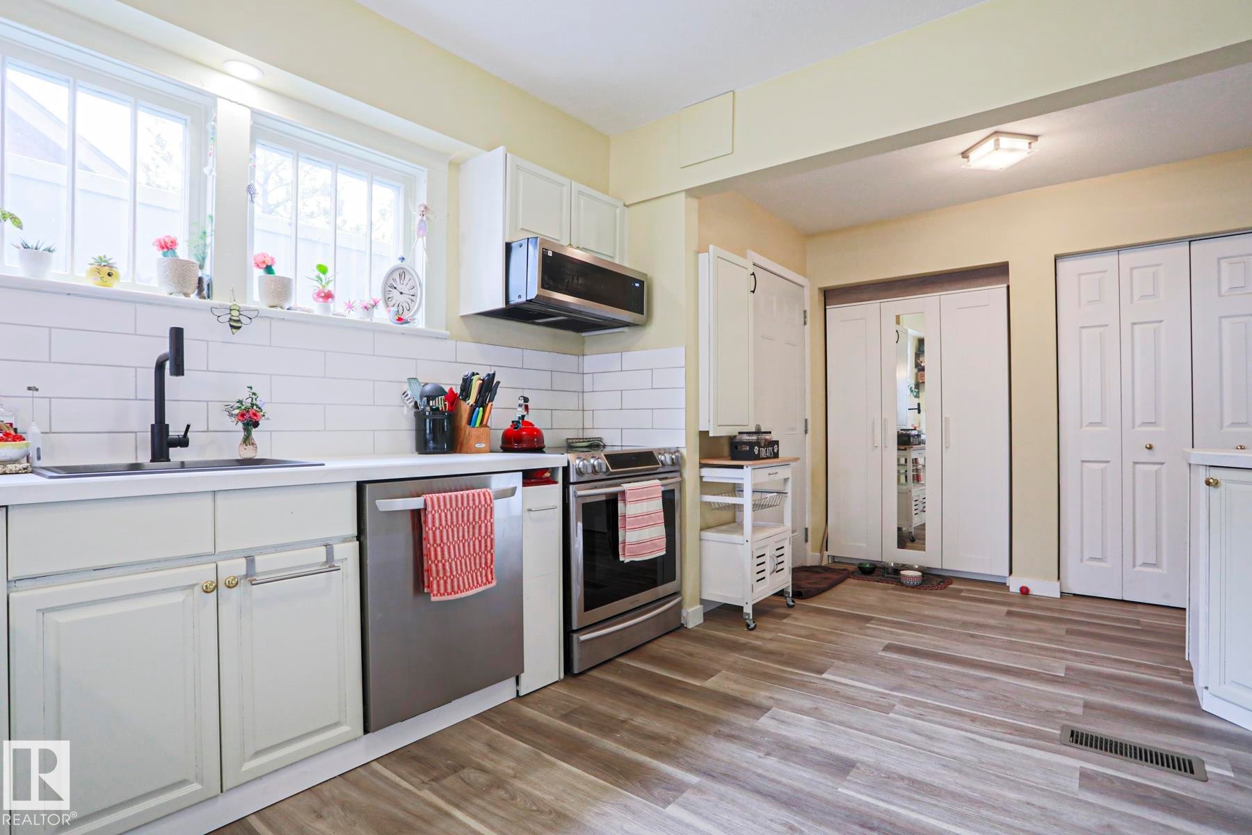 Kitchen featuring white shaker-style cabinetry, stainless steel appliances, wood-finish flooring, subway tile backsplash, and dual windows - 5113 53 Avenue, Stony Plain, AB - Indoor Photo Showing Kitchen