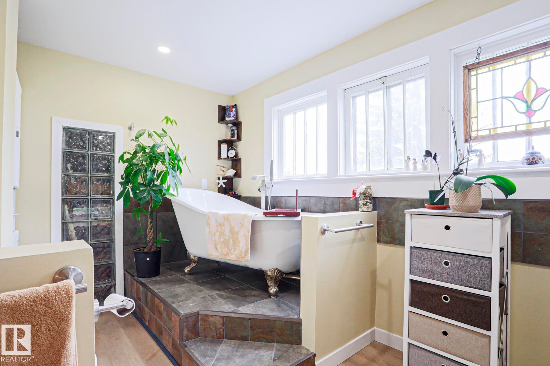 Bathroom featuring a freestanding clawfoot tub, platform with tile flooring, glass block wall, and multiple windows - 5113 53 Avenue, Stony Plain, AB - Indoor