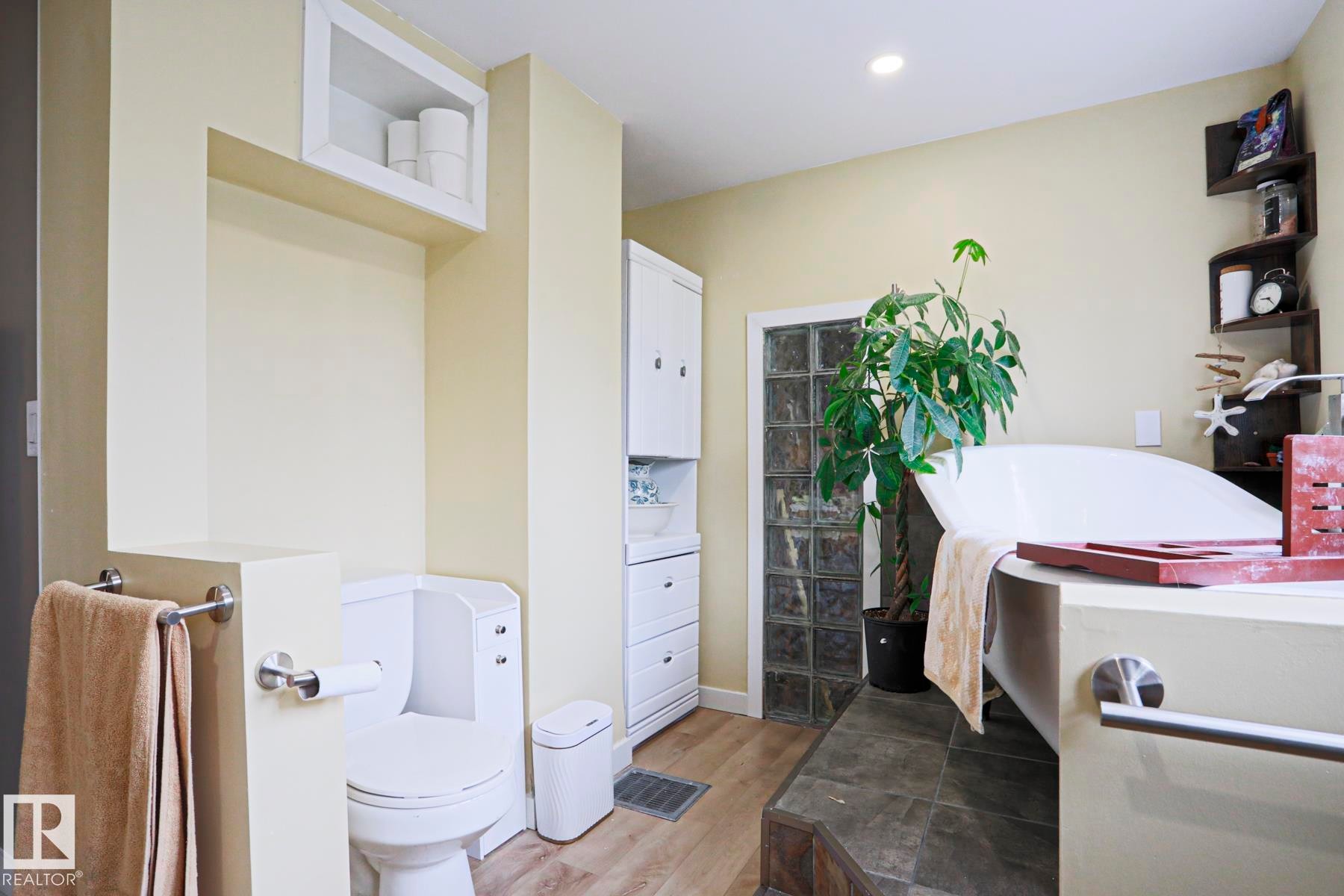 Soaking tub with integrated surround, glass block window, built-in shelving, wood-finish flooring, and recessed lighting - 5113 53 Avenue, Stony Plain, AB - Indoor